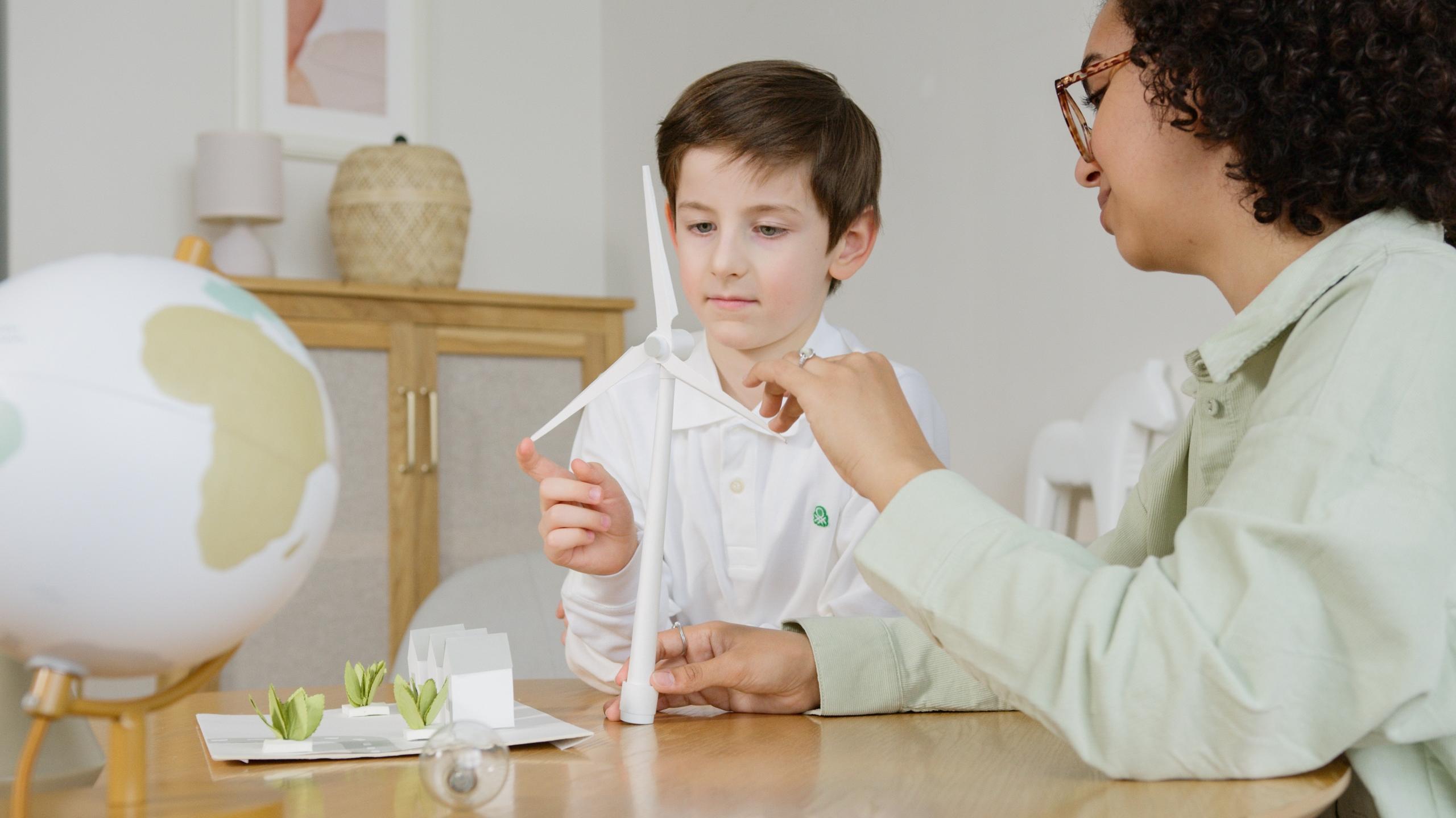A tutor works with a child using models of a windmill and a globe.