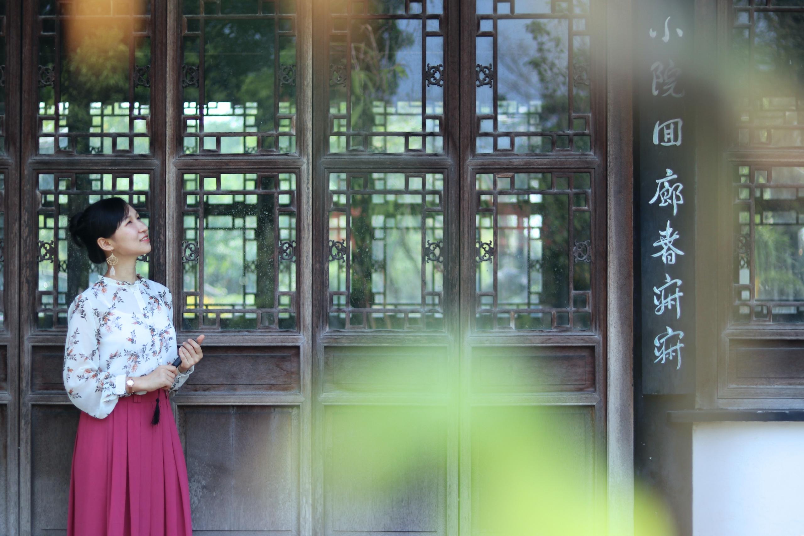 A woman stands outside a building with Chinese writing.