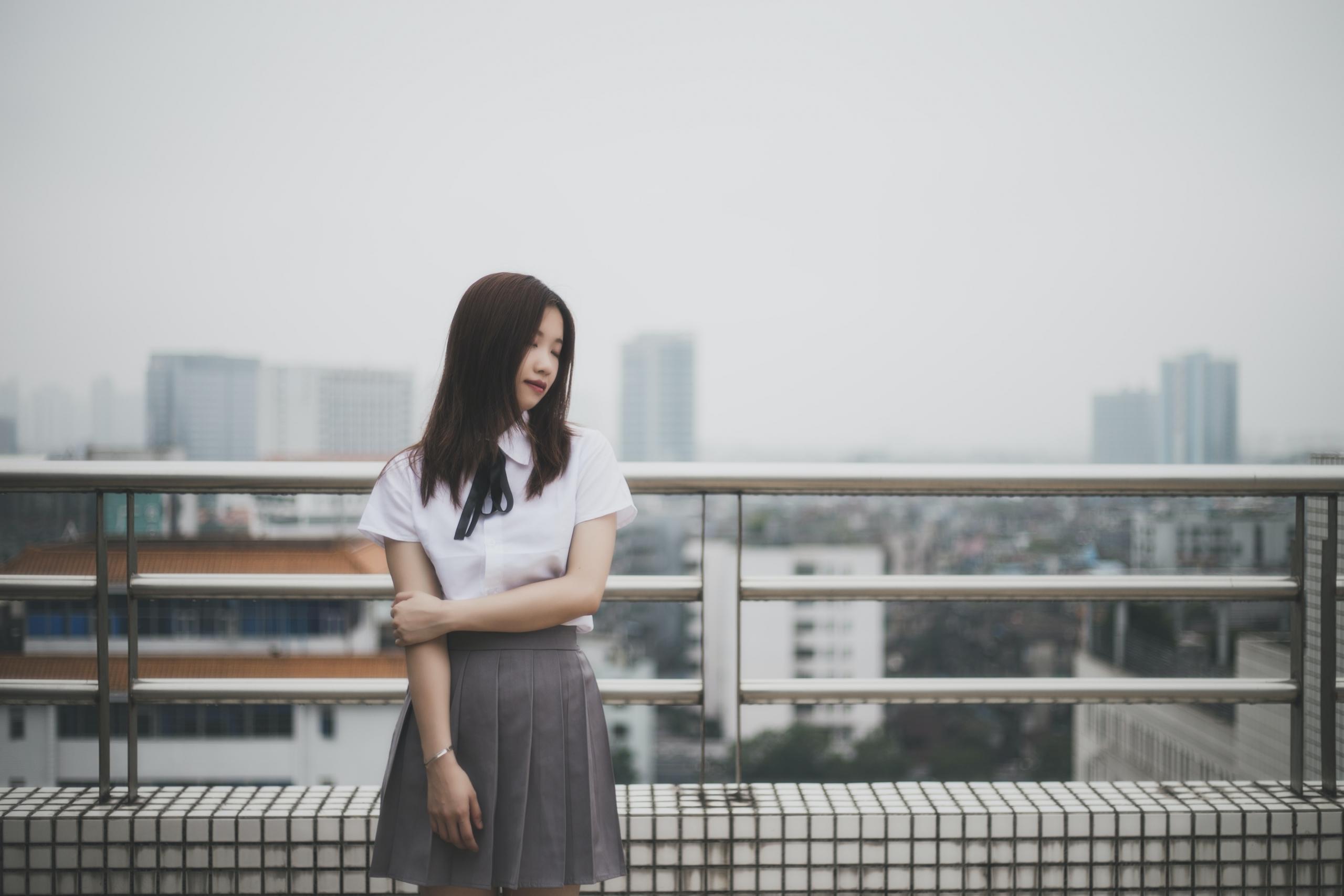An Asian woman stands on a balcony overlooking the city.