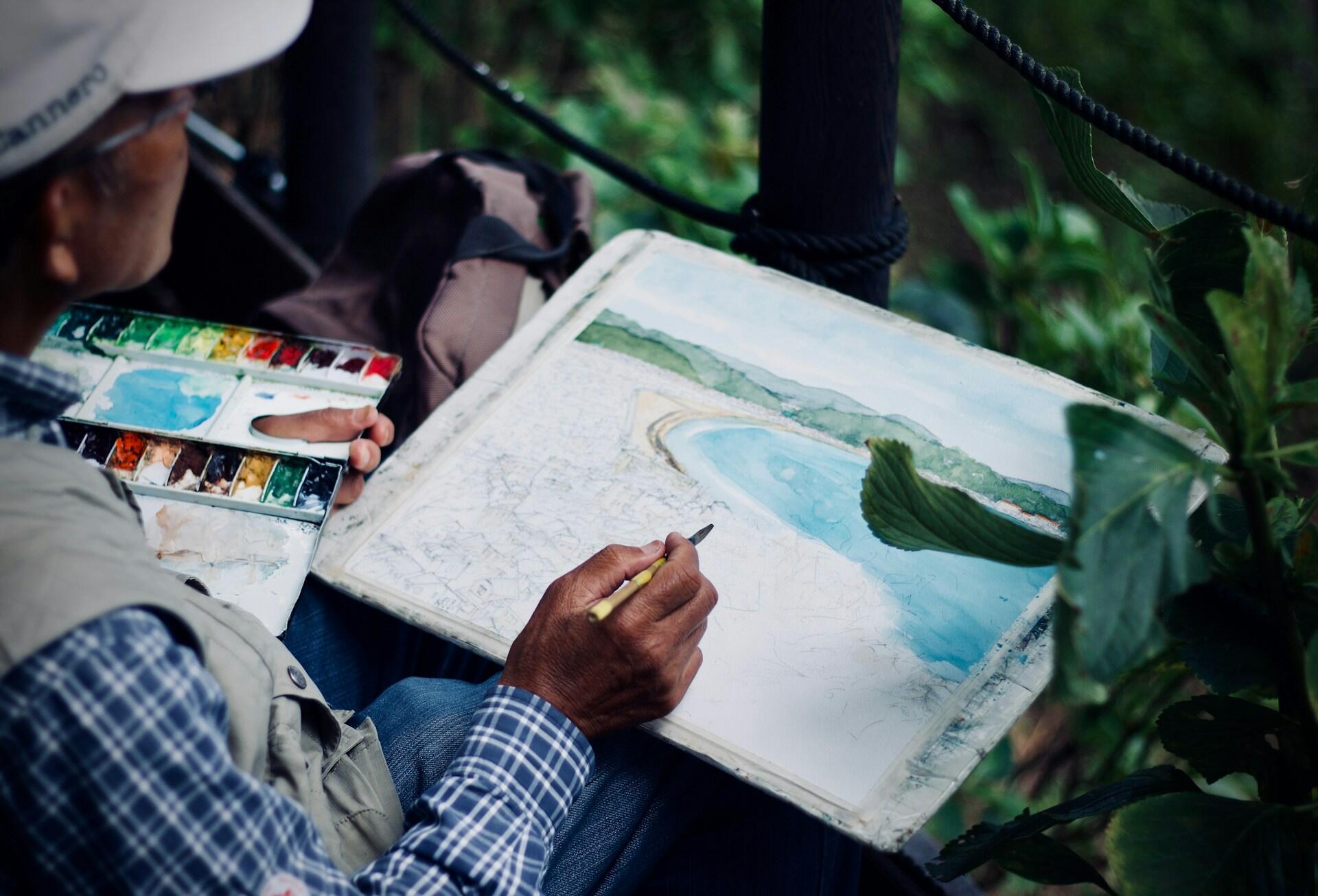 Artist painting a landscape with watercolors outdoors.