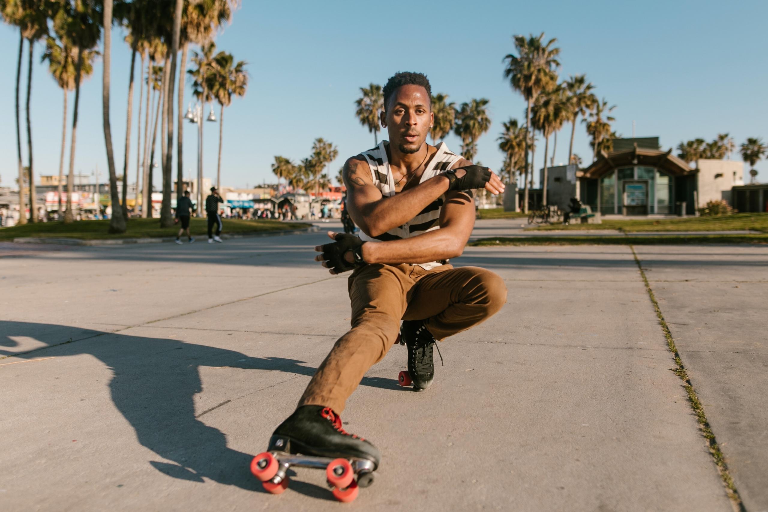 A man poses with roller skates in front of palm trees.