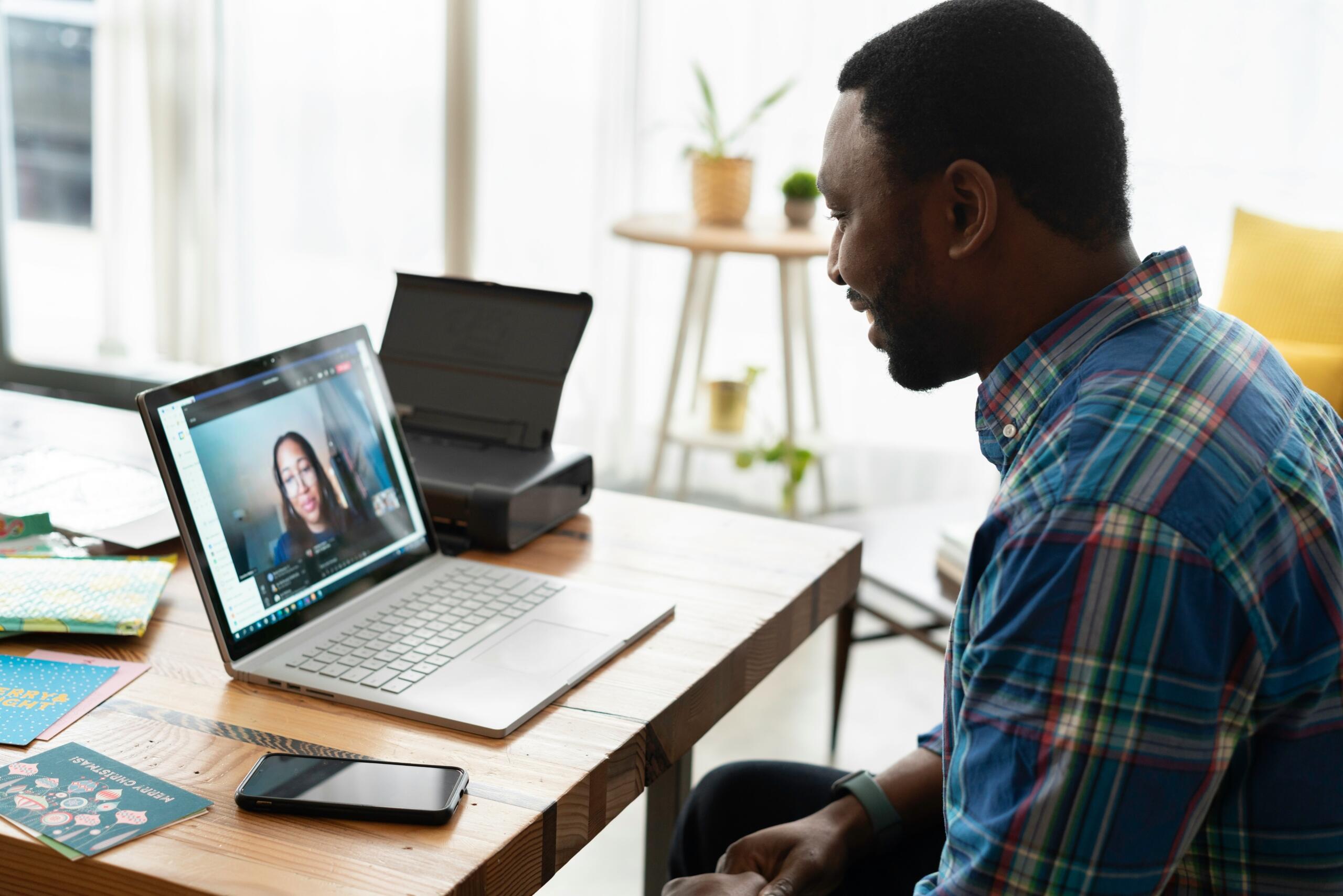Man attending an online tutoring session via laptop, speaking to a female tutor on a video call at a home desk.