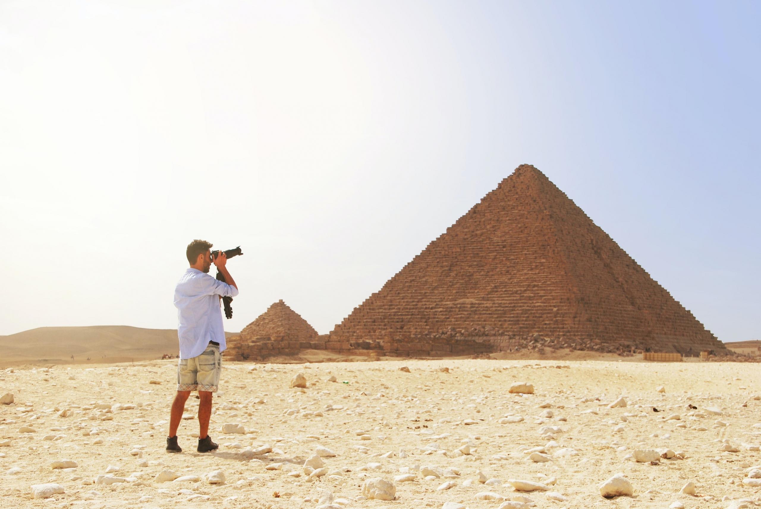A man gazes at the great pyramids of Giza. He holds a long range camera and takes a photo.