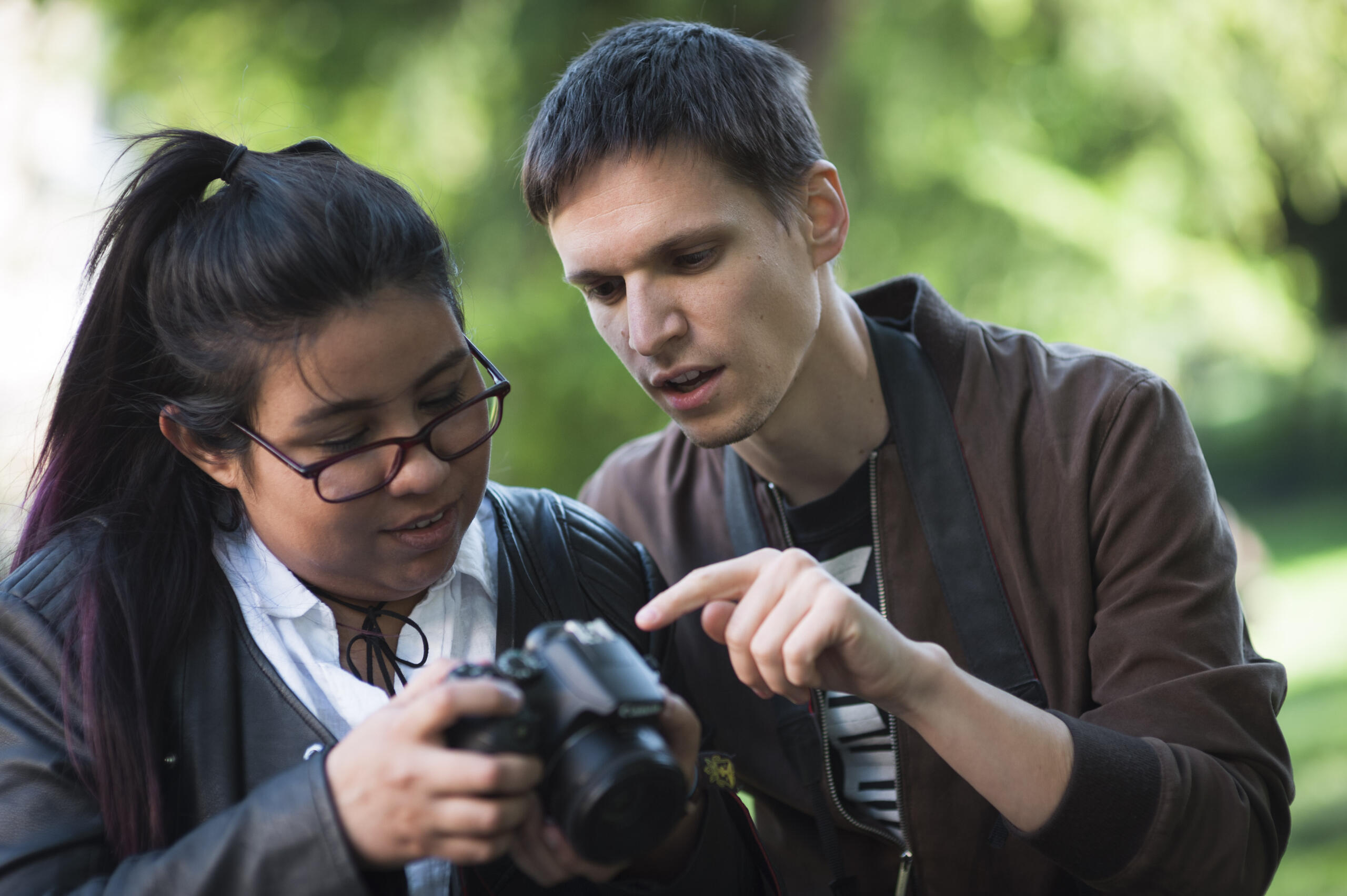 Male photography tutor showing a female student how to use a DSLR camera during an outdoor lesson.