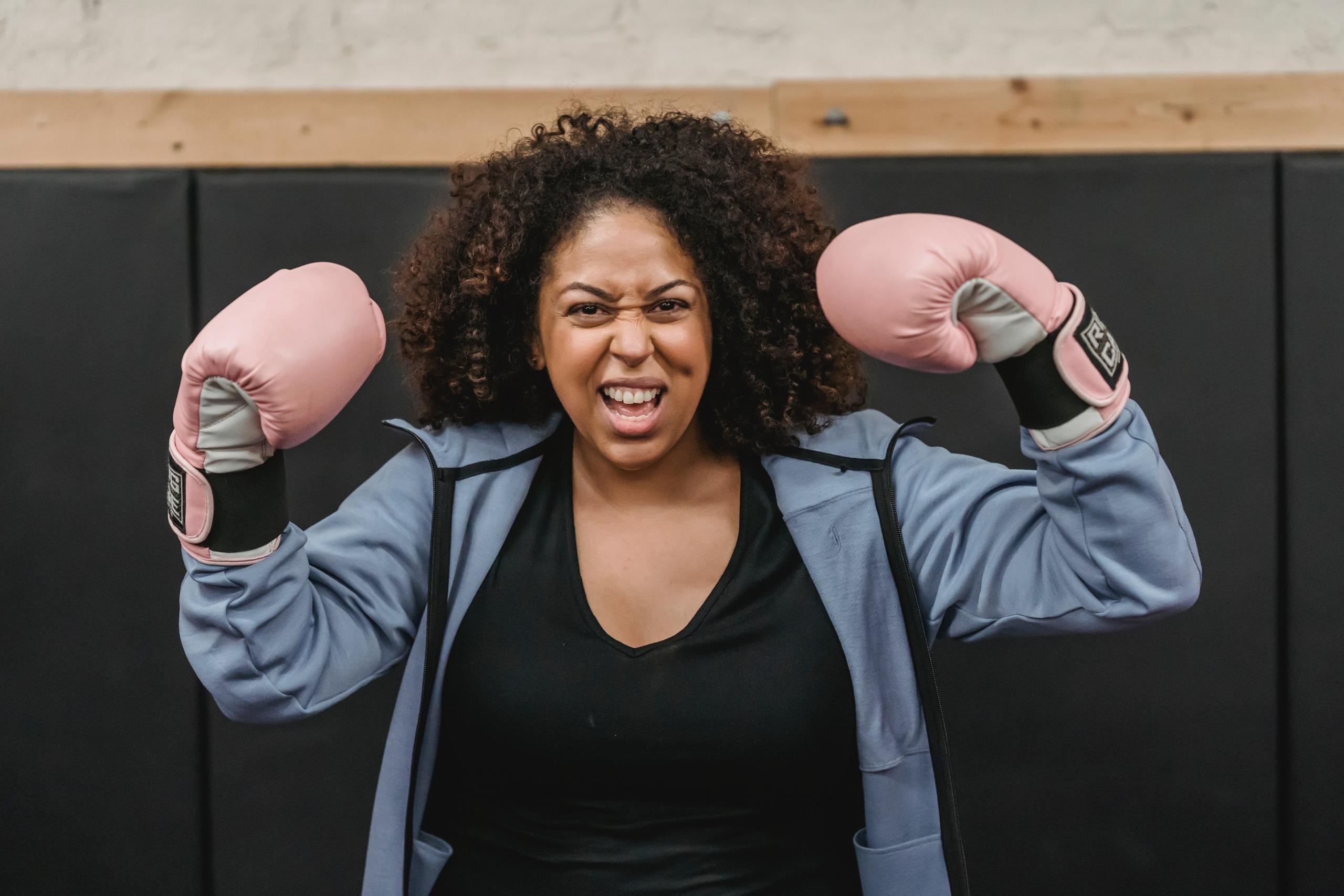 A woman in a blue shirt wears pink boxing gloves.