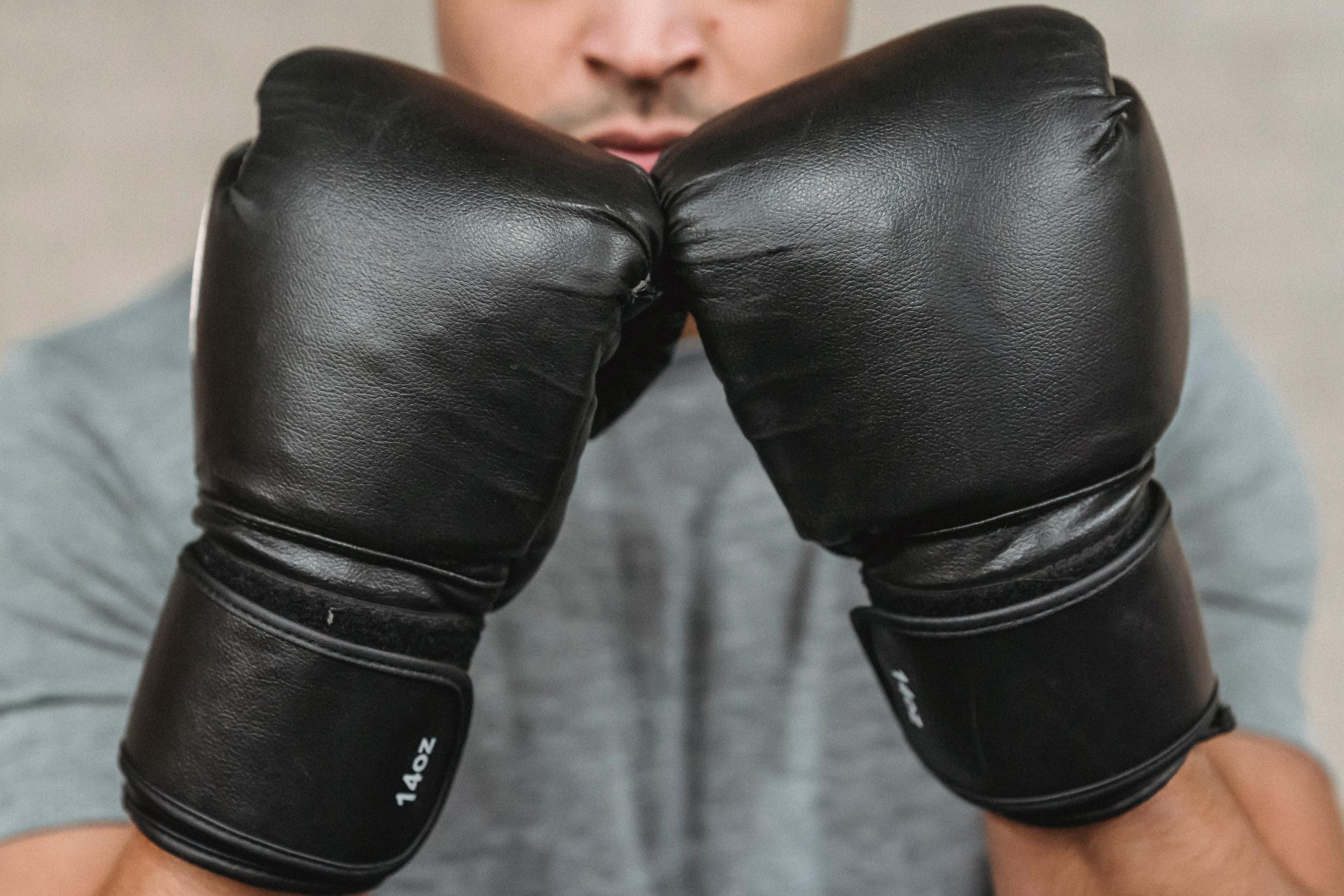 A man wears a pair of black boxing gloves.