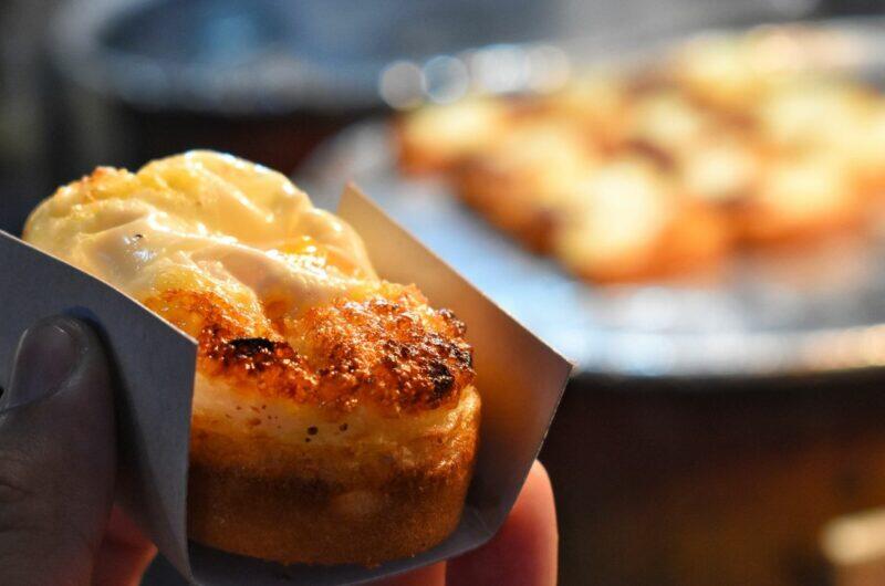Close-up of a freshly baked Korean egg bread (gyeranppang), showing its golden, slightly caramelized top and soft, fluffy texture, held in a paper wrapper at a street food stall.