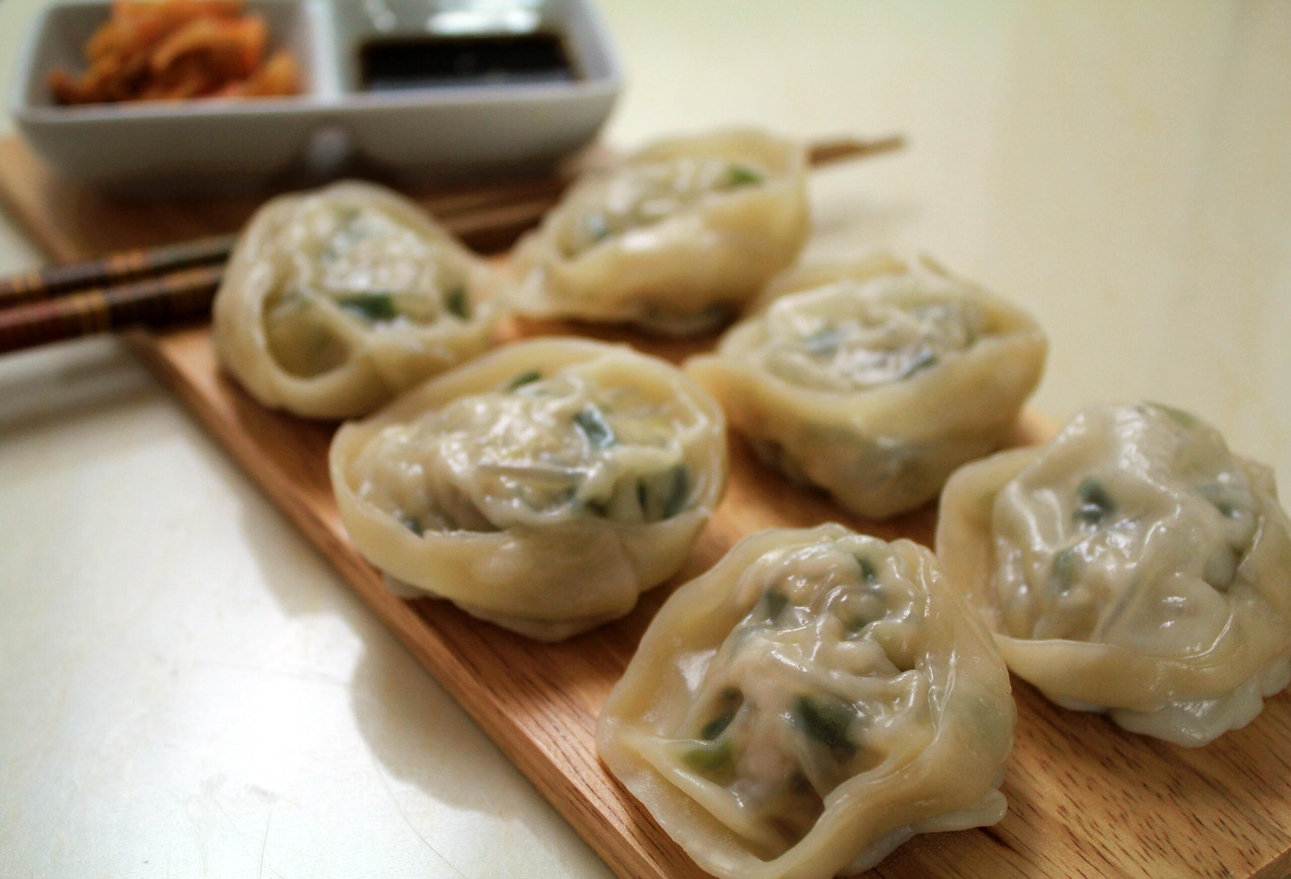 Close-up of Korean mandu dumplings neatly arranged on a wooden board, filled with minced meat, vegetables, and noodles, served with soy sauce and kimchi on the side.