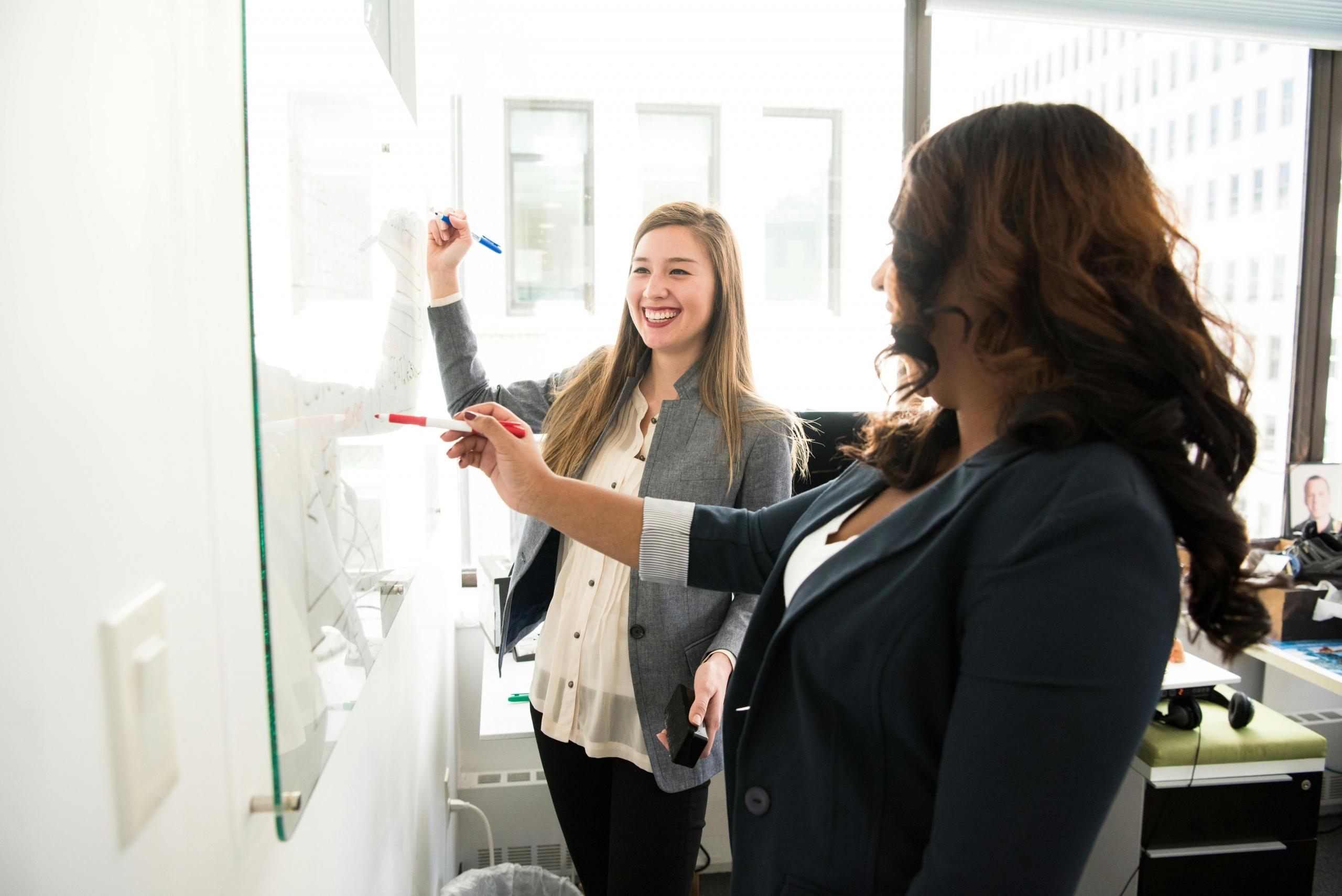 two professionals stand in front of a white board.