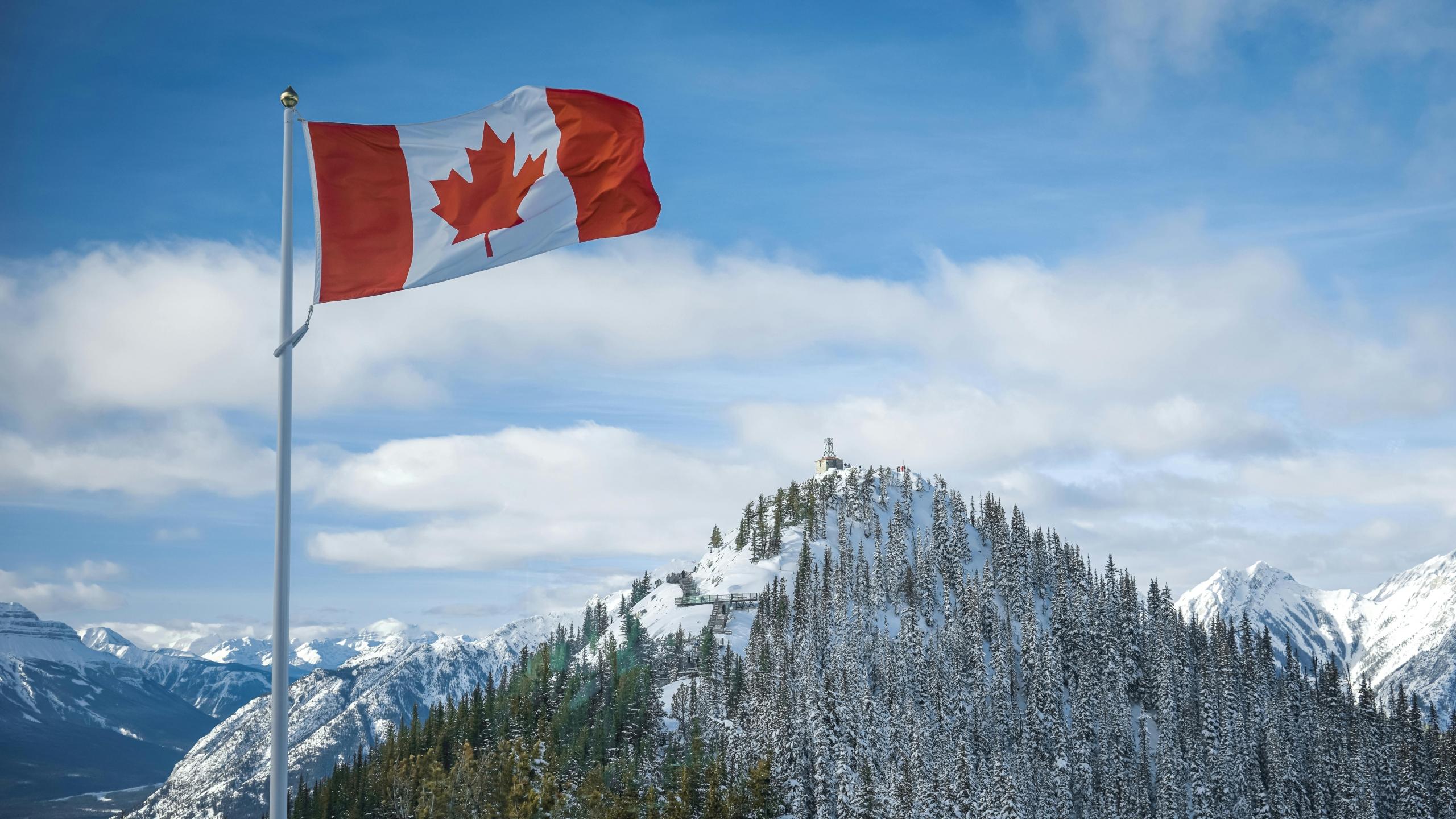 A Canadian flag flies over a mountain.