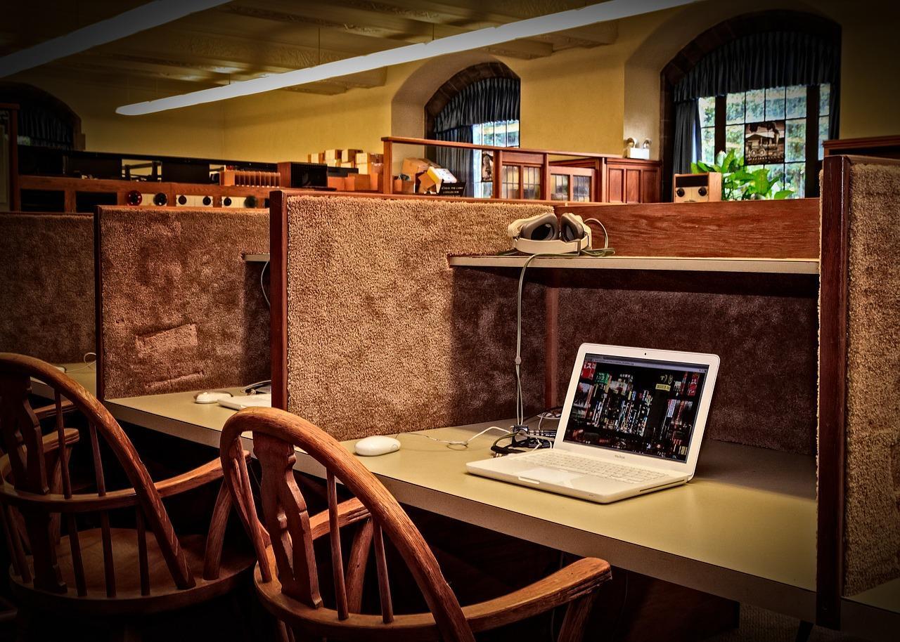 Study cubicle with a laptop, headset, and reading glasses in a quiet library setting.