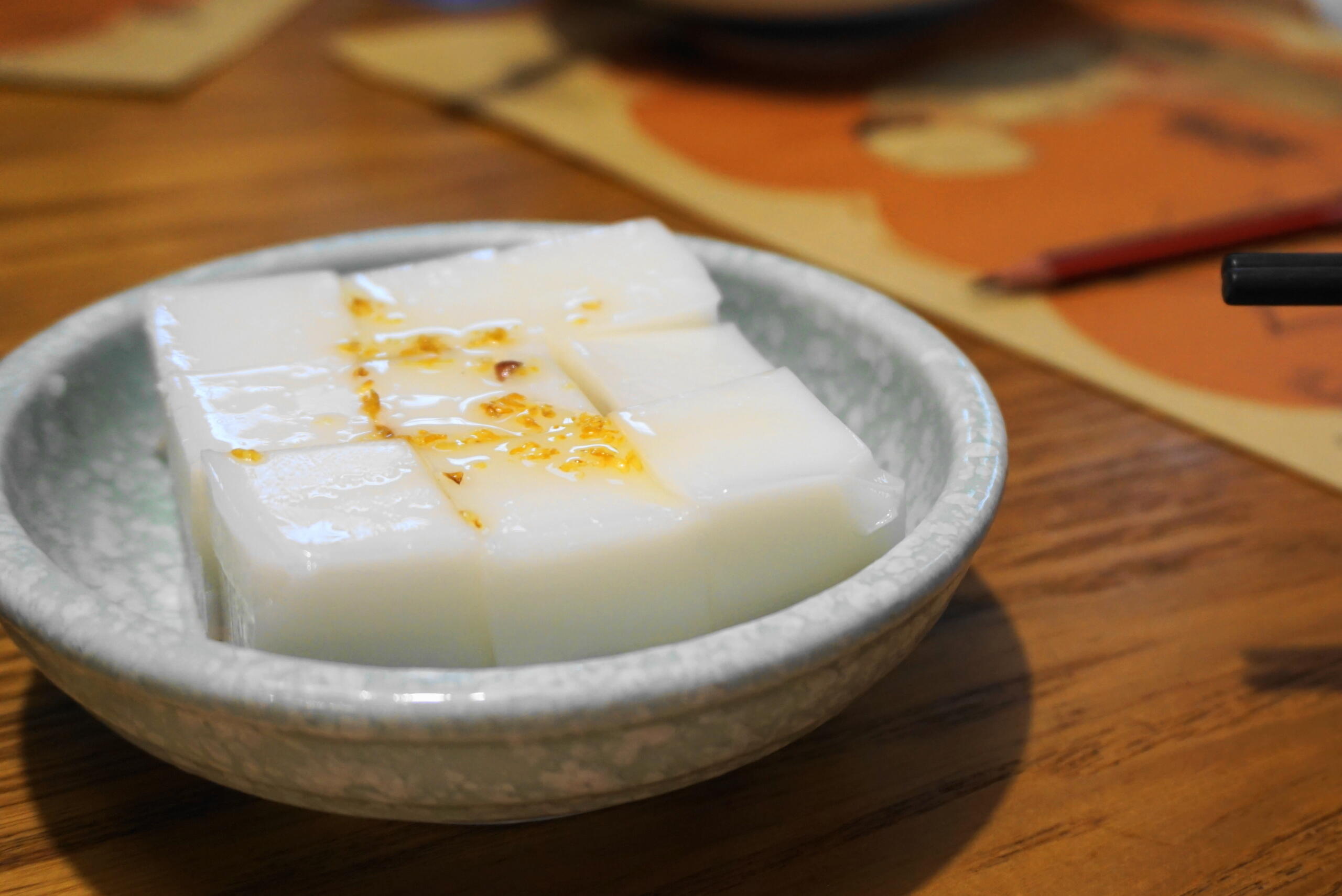 A small grey plate/bowl of almond tofu (Xing Ren Dou Fu) on a wooden table.