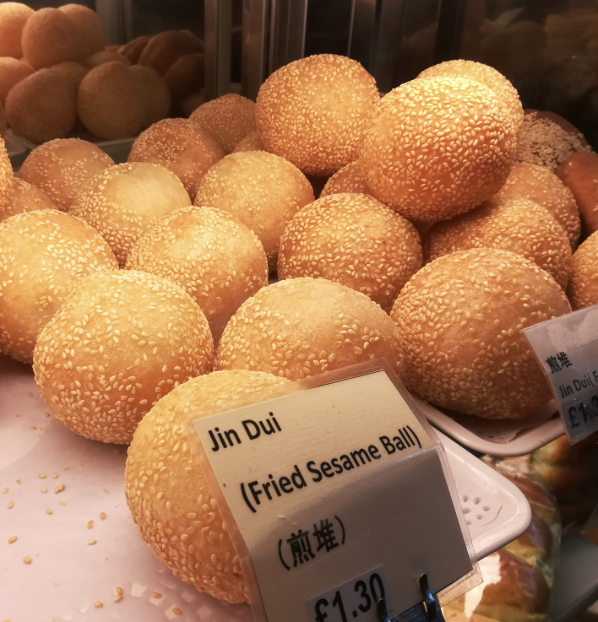 A close-up of golden fried sesame balls stacked on a tray, labeled "Jin Dui (Fried Sesame Ball)" priced at £1.30.