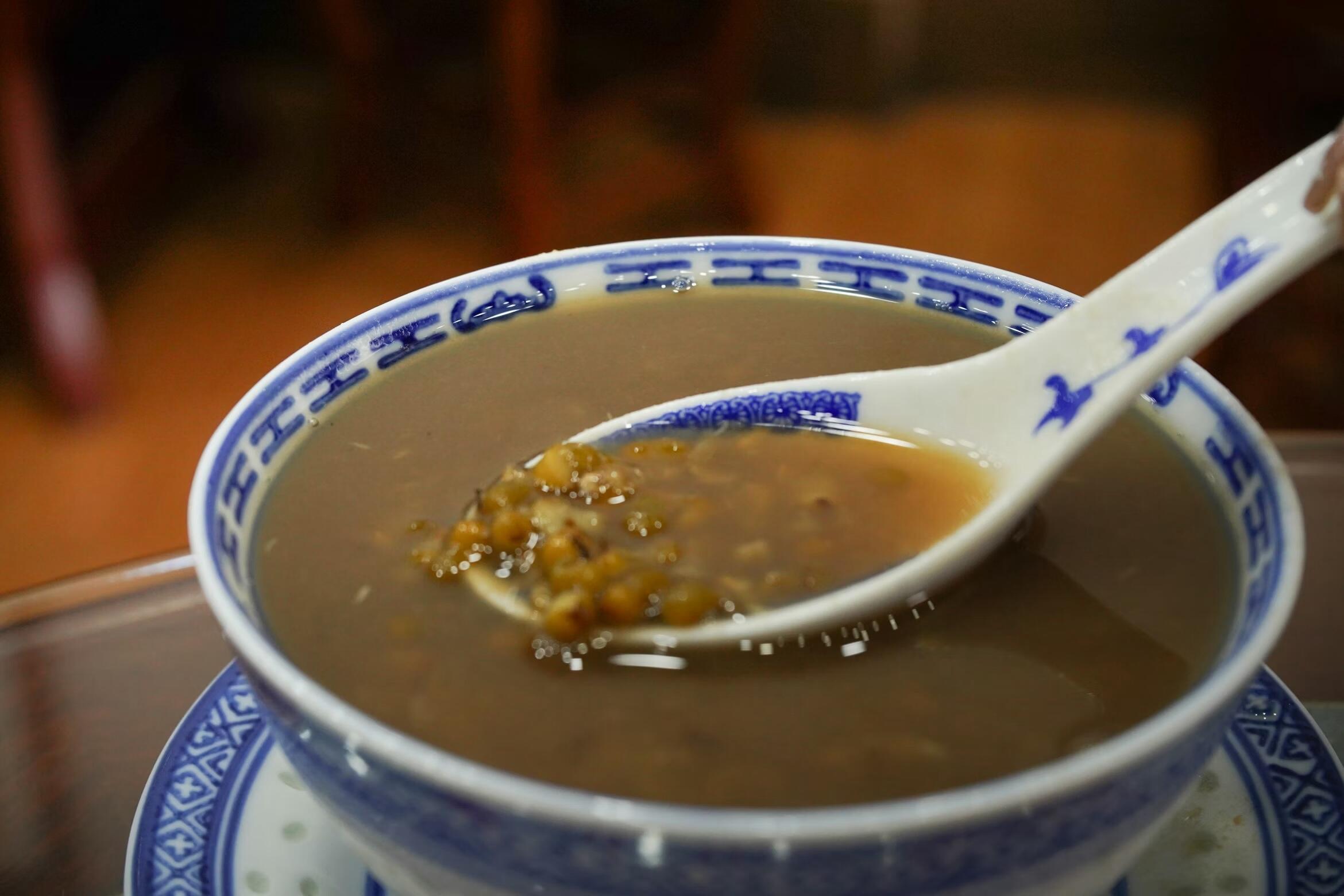 A spoon scoops thick, brown soup from a bowl adorned with blue patterns, set on a wooden table.