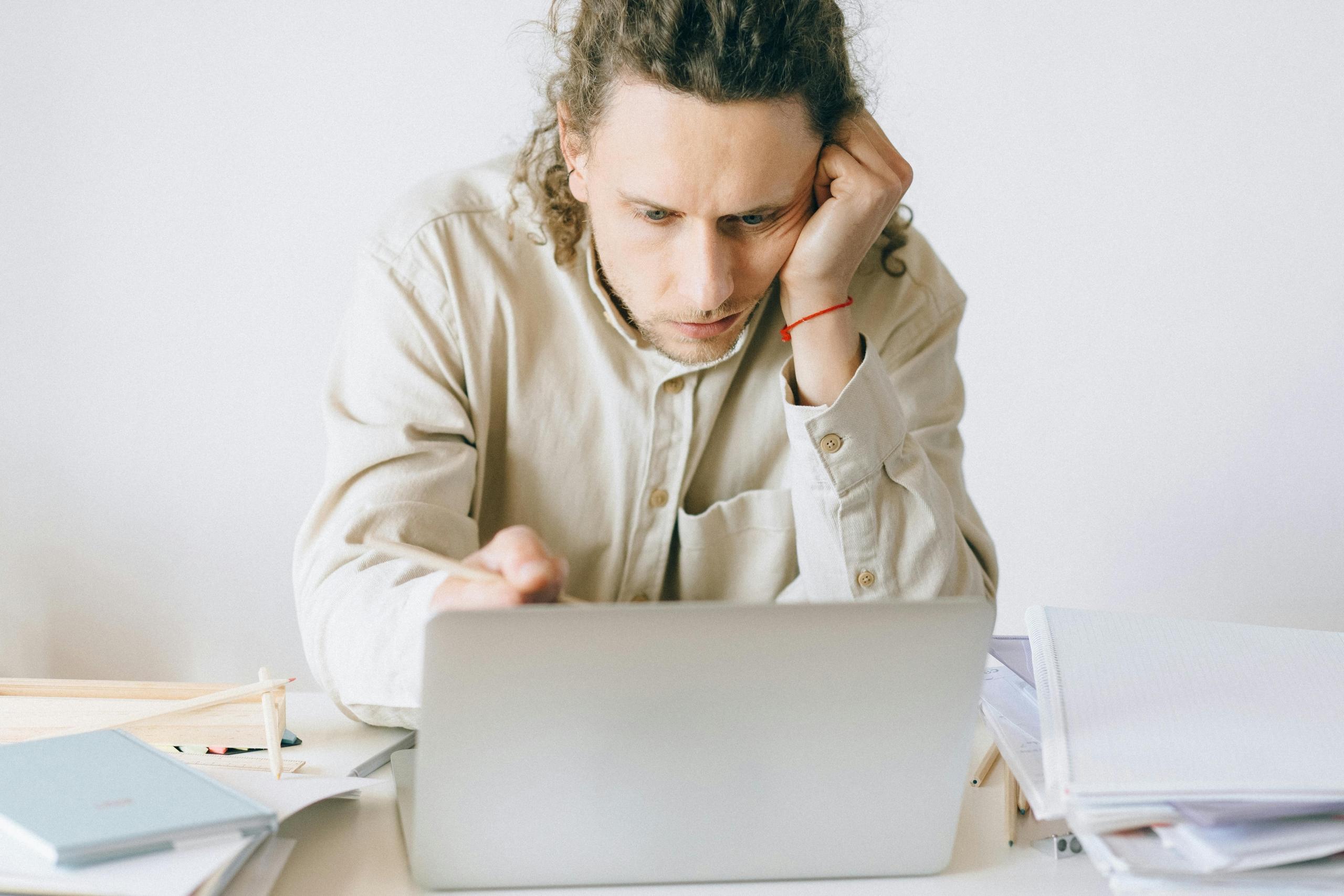 a man looks at a computer while writing with his head in his hands.