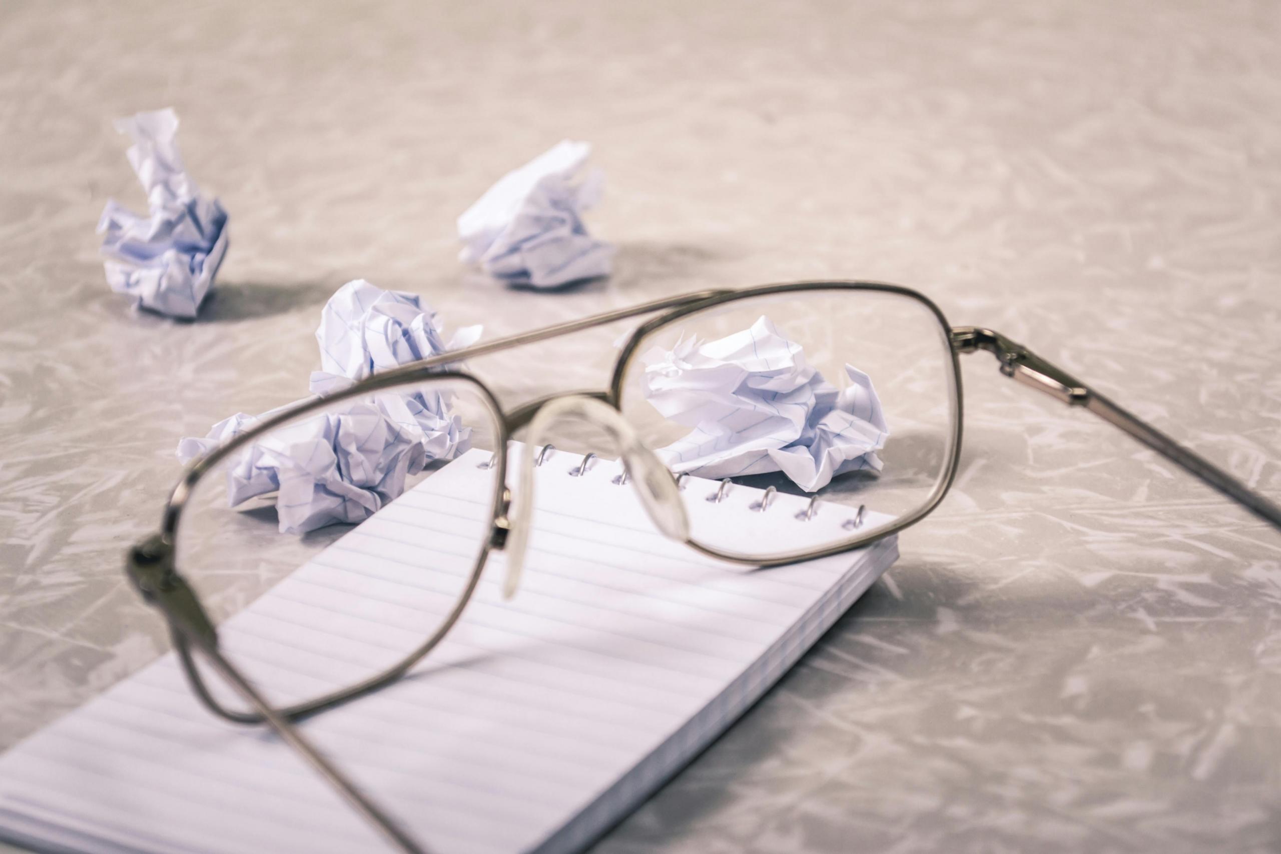 crumpled paper sits beside an empty notebook and glasses.