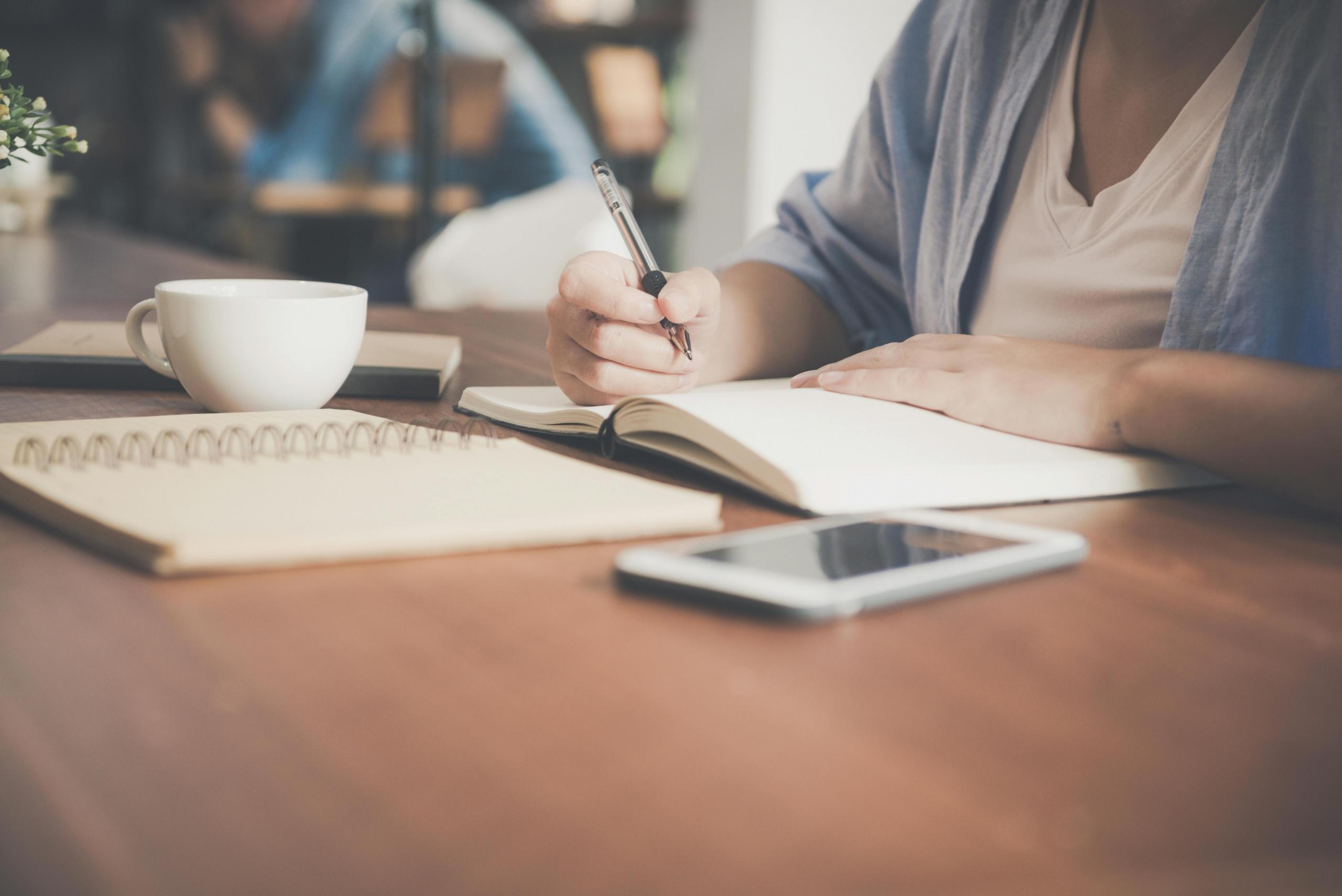 a student writes at a table. A mug is on the table.