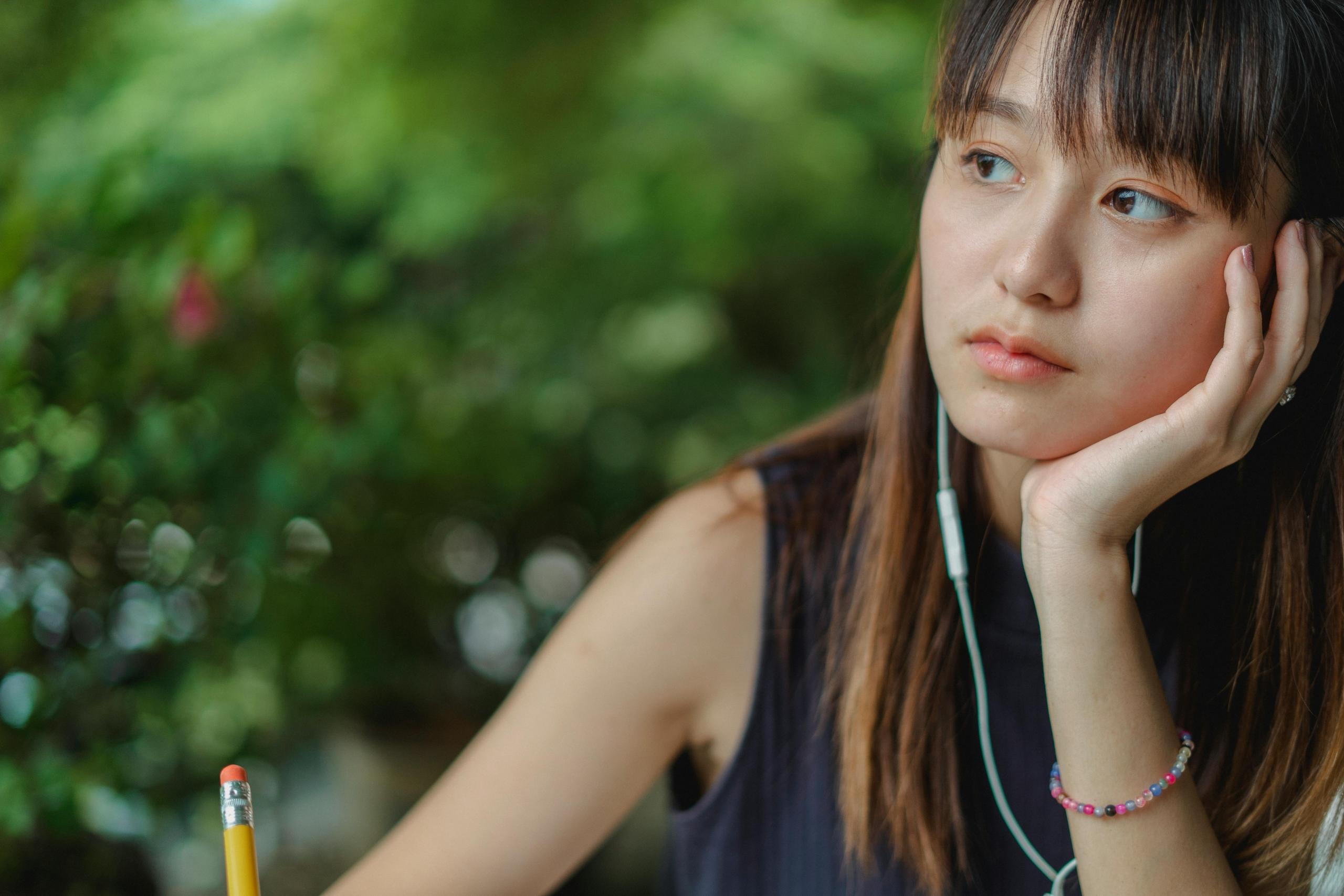 A woman looks in the distance while holding a pen and listening to headphones.