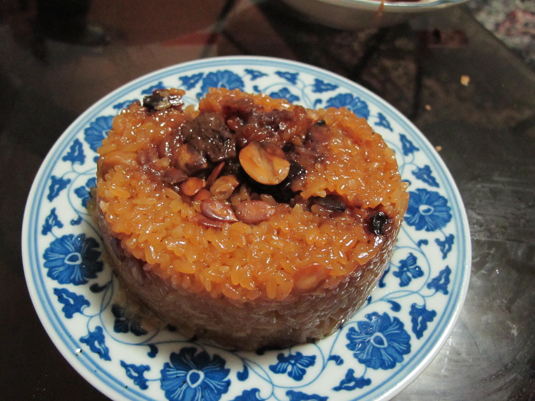 A plate of sticky rice cake topped with nuts and sweet sauce, served on a blue floral-patterned dish.