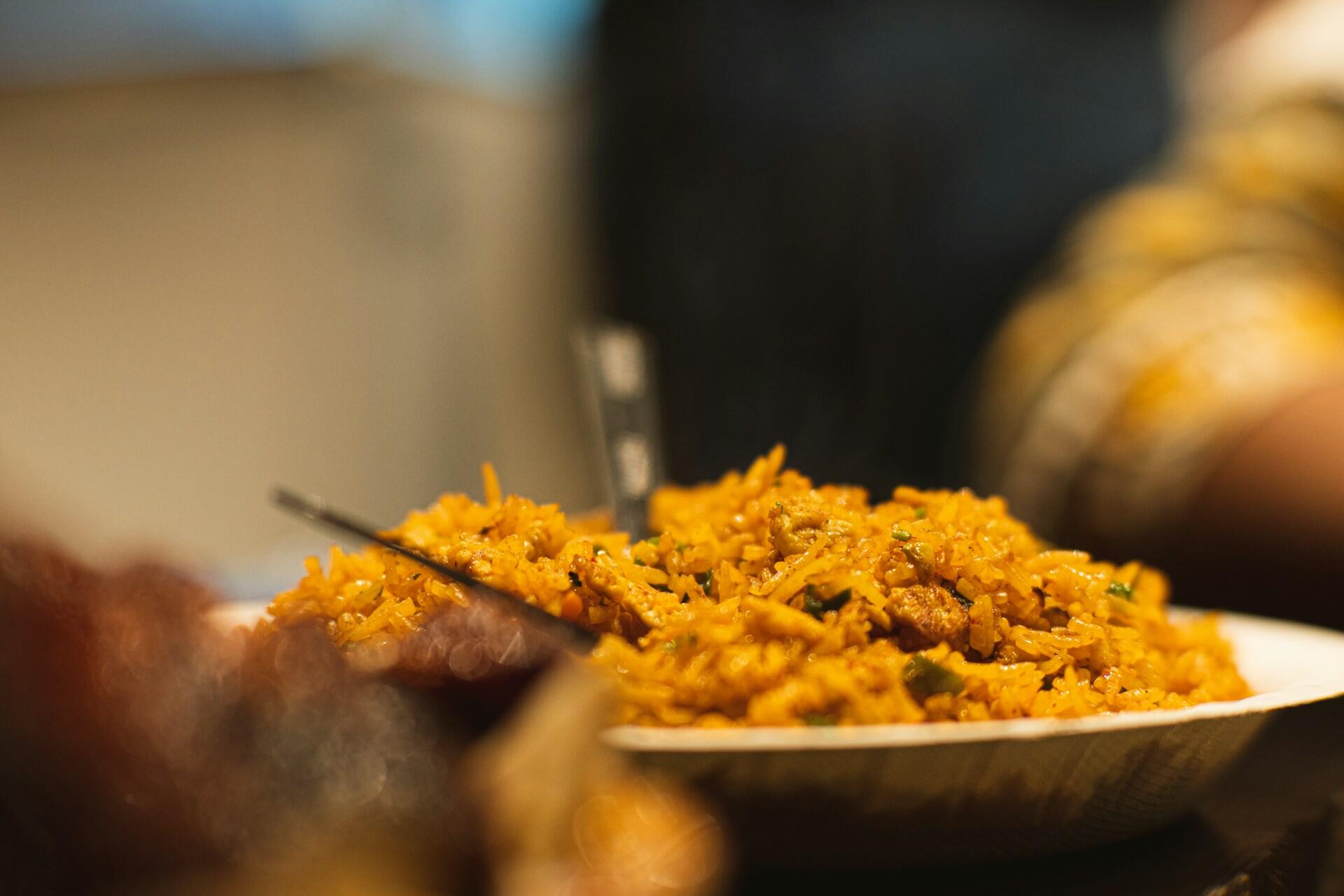 Plate of spicy yellow rice with vegetables and meat, with a spoon inserted, photographed with a shallow depth of field.