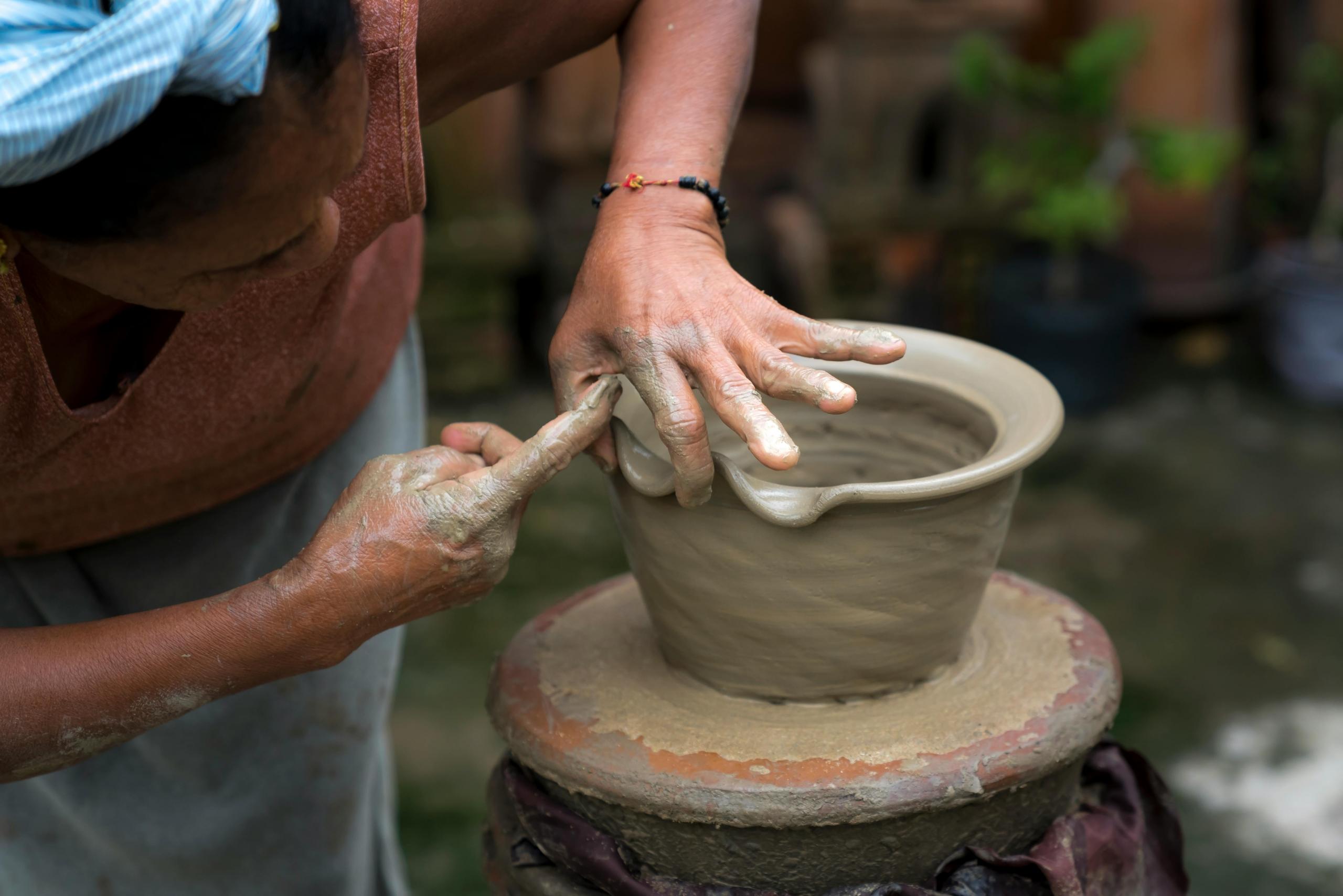 a woman uses her hands to shape the rim of a clay pot.