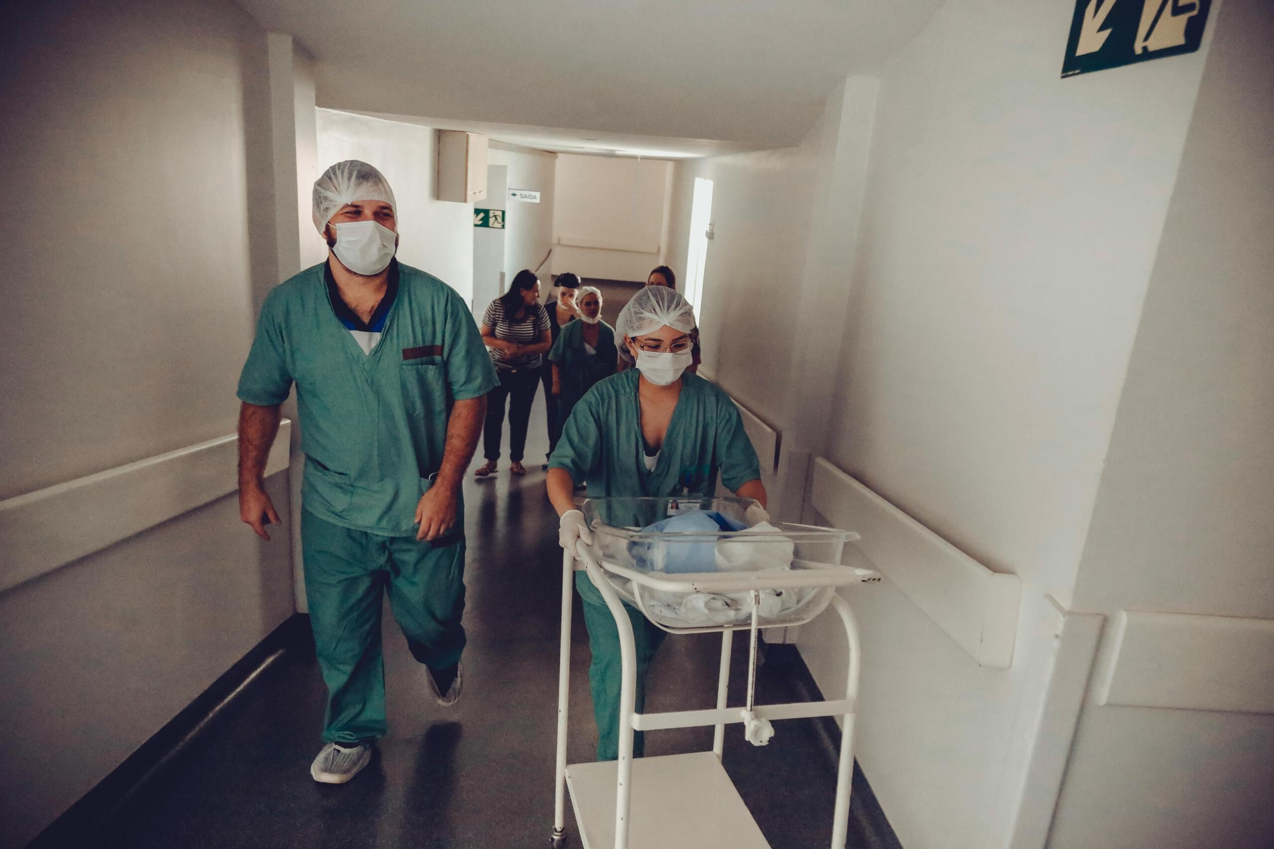 nurses push a newborn in a cot through hospital corridors.