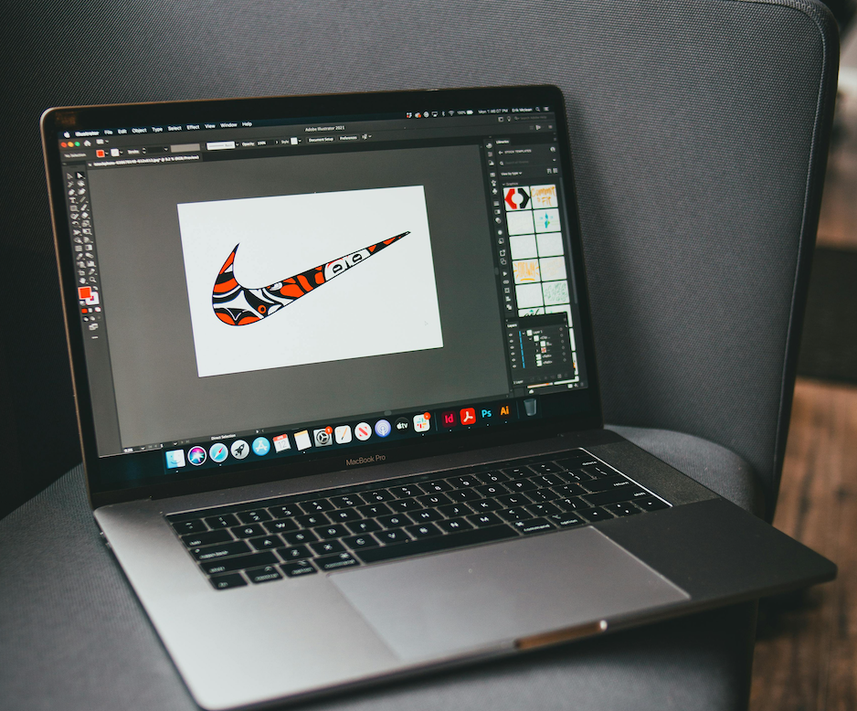 Laptop placed on a sofa. It shows the program InDesign by Adobe and presents a modified Nike logo in orange, black and white.