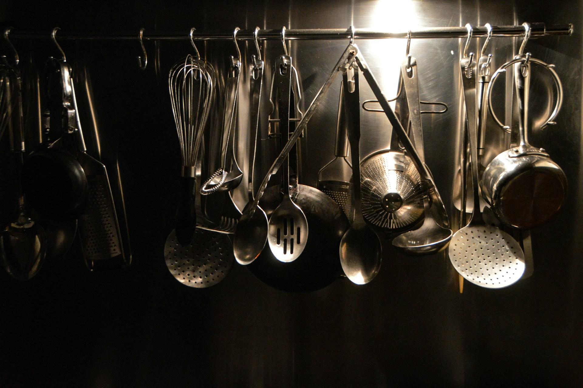 Multiple culinary utensils, like whisks, cheese graters and spoons, handing on the wall.