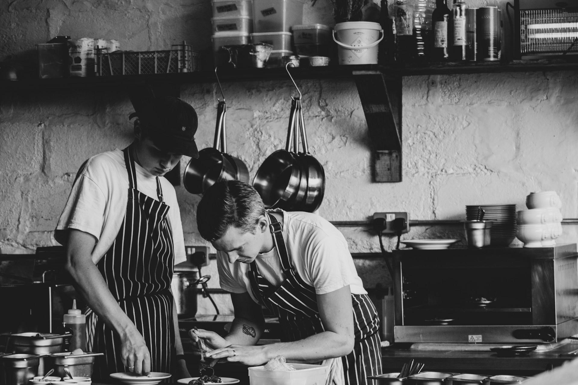 two young chefs plating a dish in the kitchen