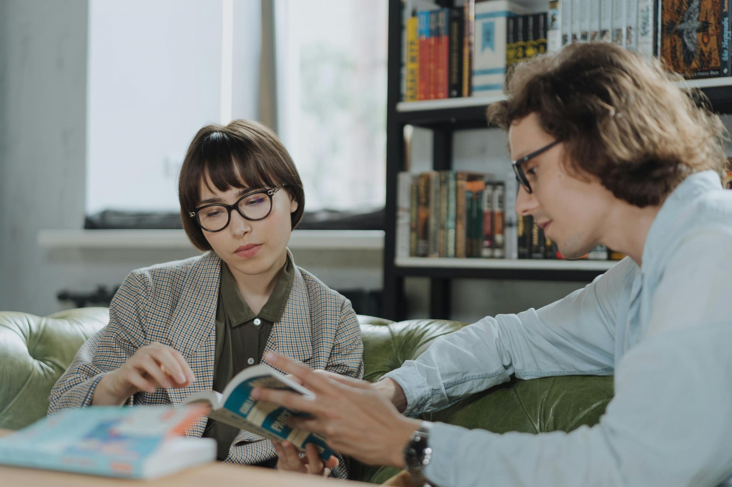 a man and woman sit together and look at a book.
