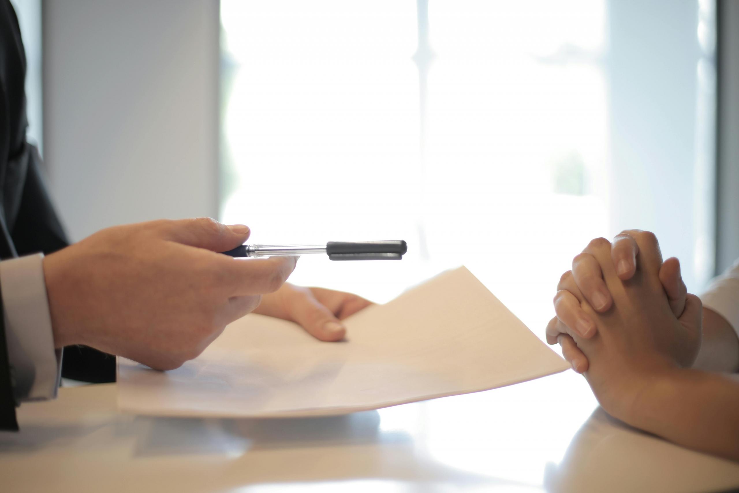 A man holds a pen and a sheet of paper to another person.