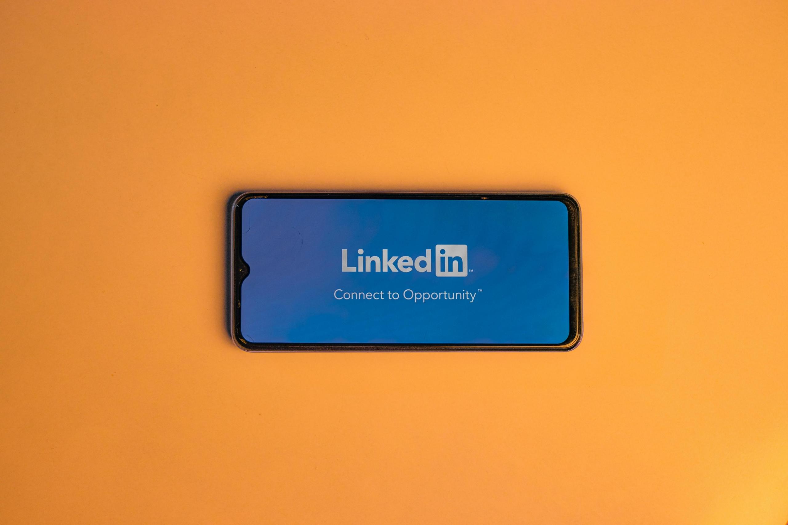 Orange background with a phone showcasing the LinkedIn logo and slogan.