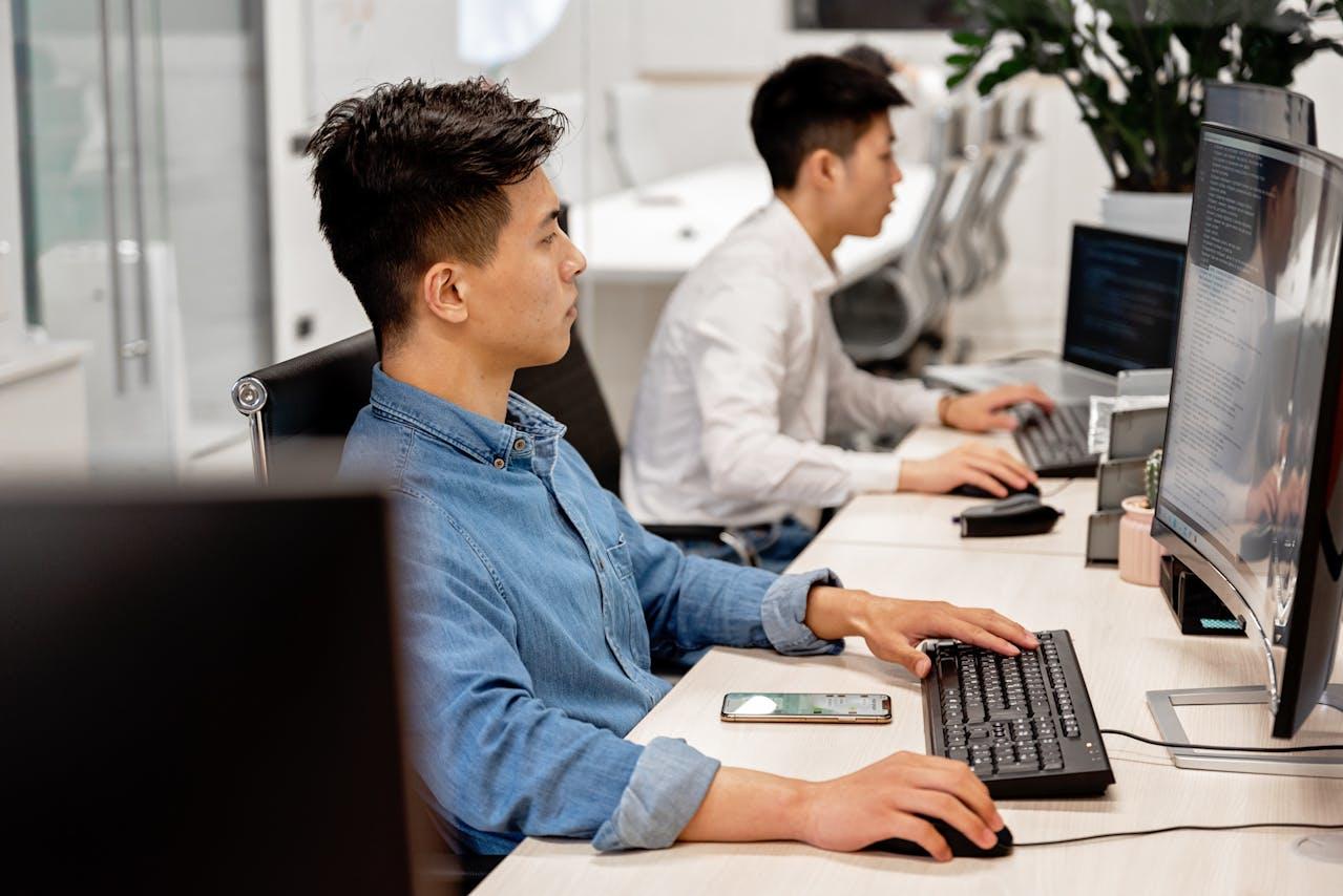 2 men working at a desk reading code on a computer
