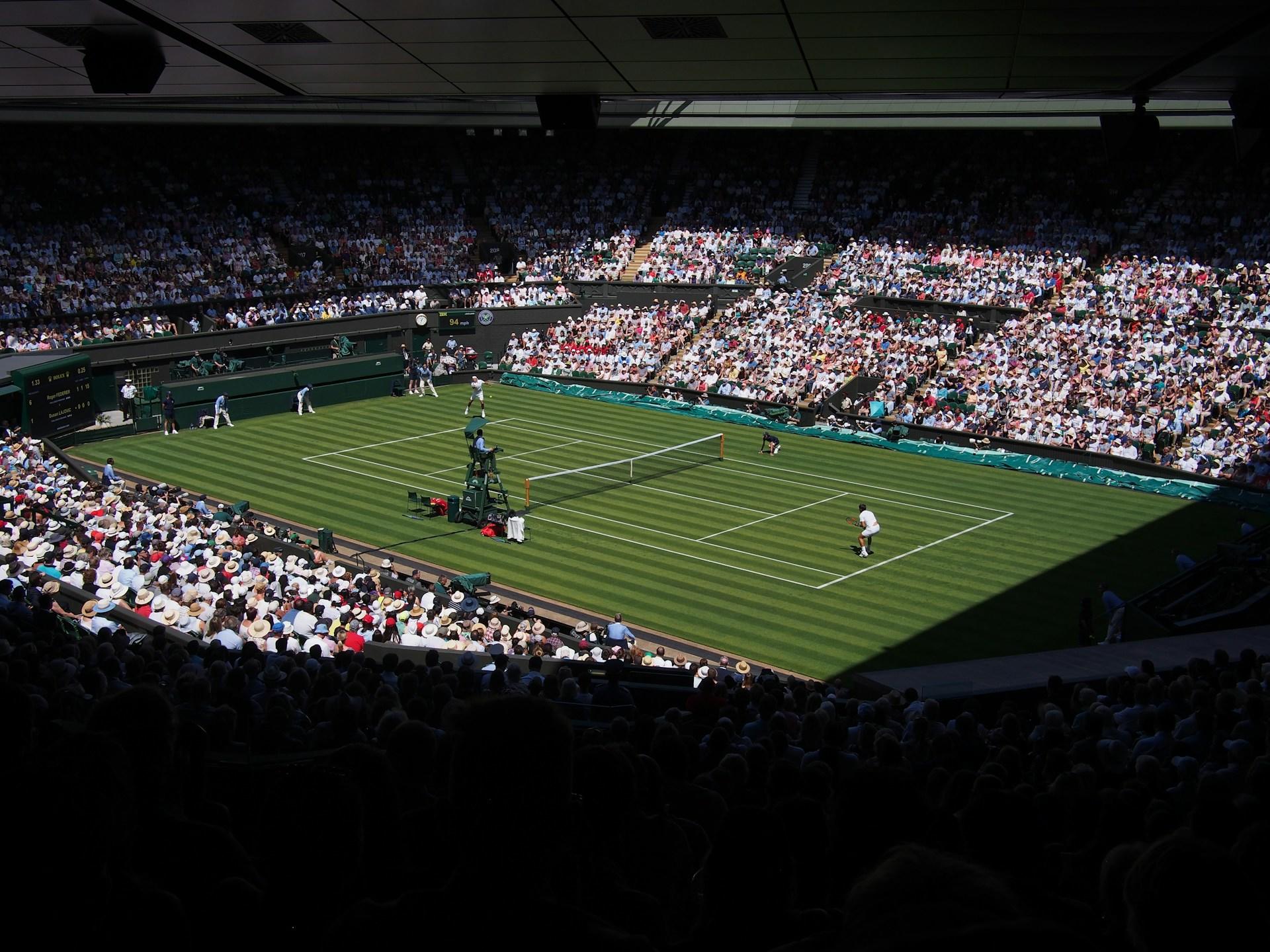 A tennis match in Wimbledon with a full house of expectators. 