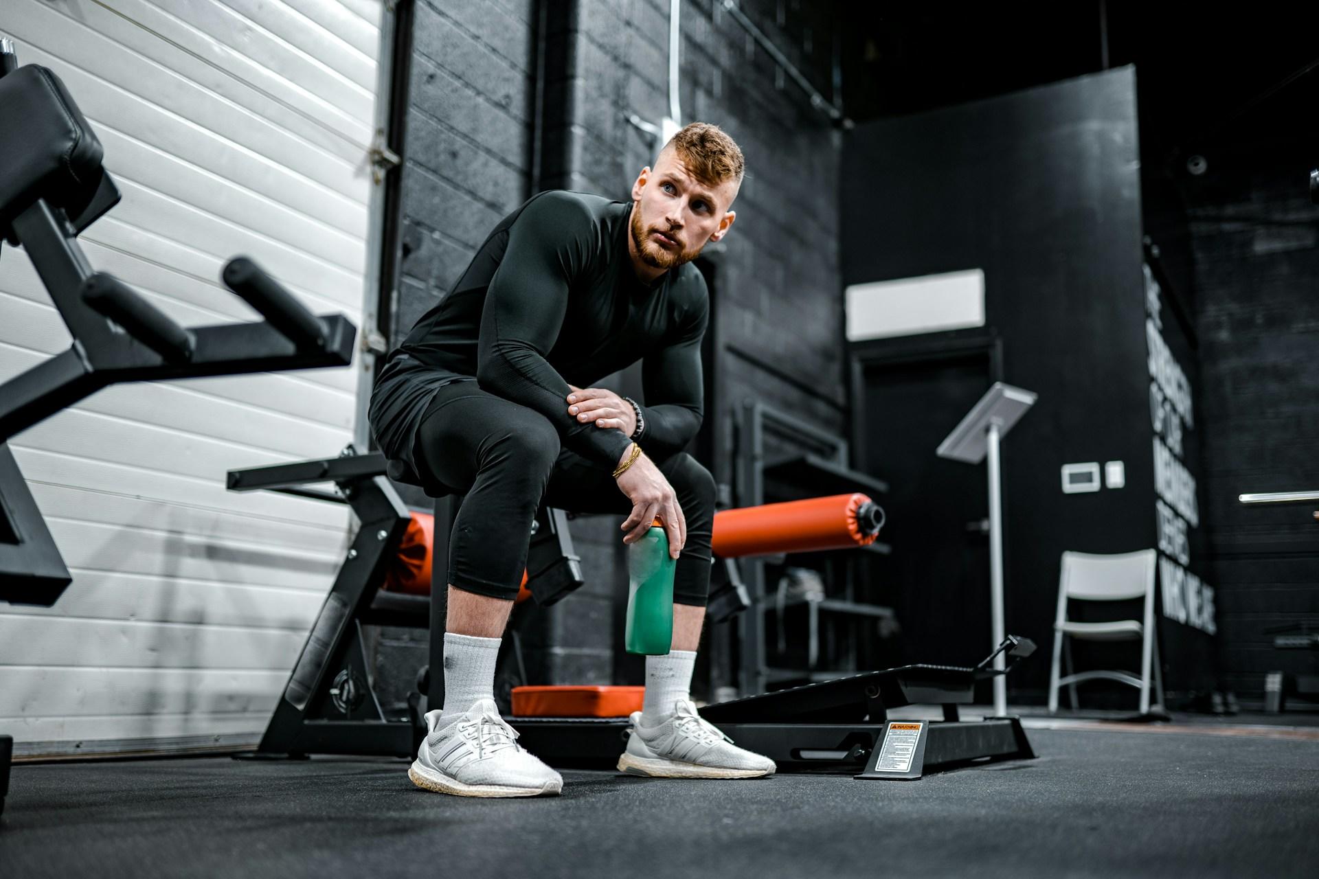 A man enjoying his break from calisthenics while sitting on a machine at the gym.