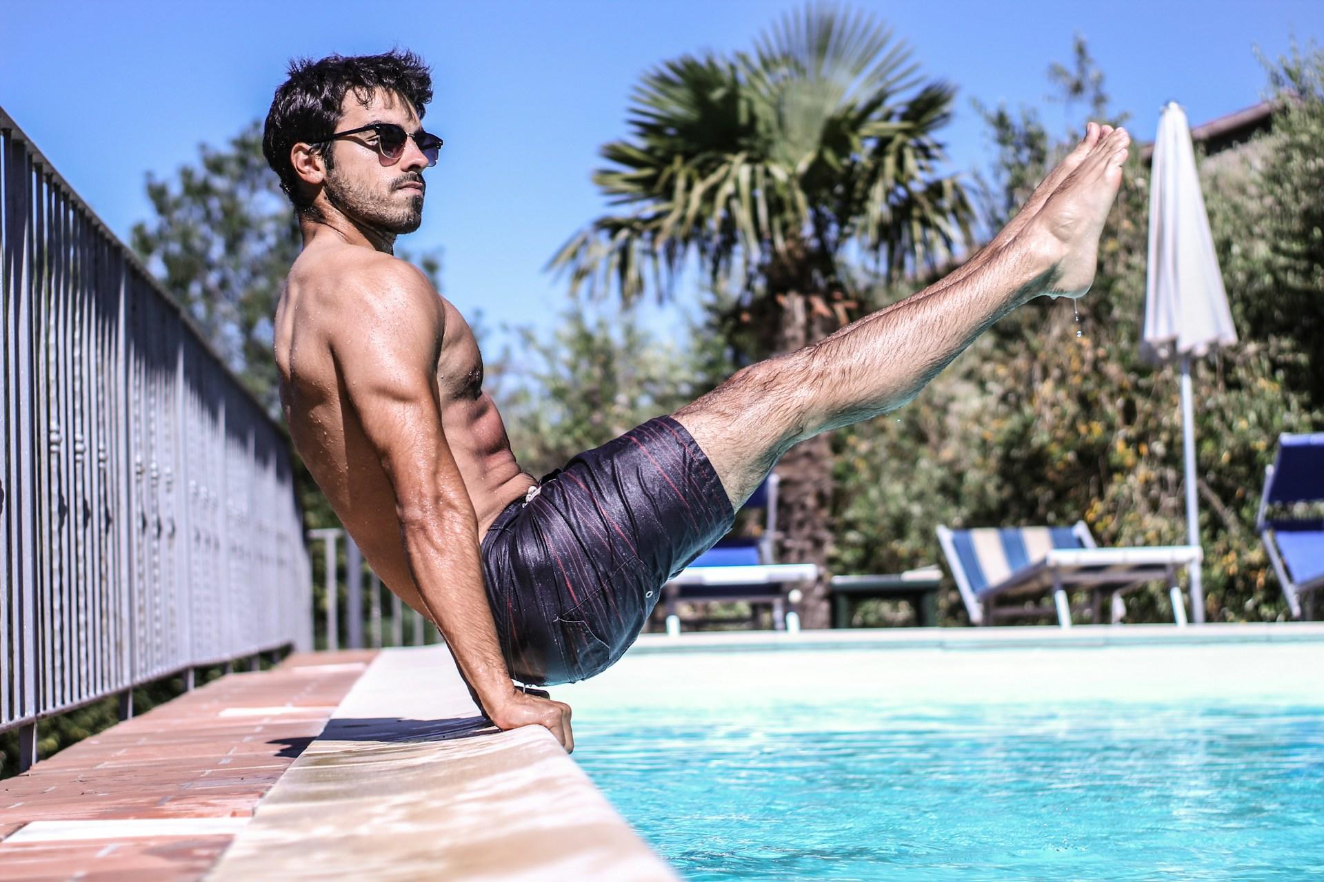 A man practising his calisthenics skills by the pool, enjoying himself.