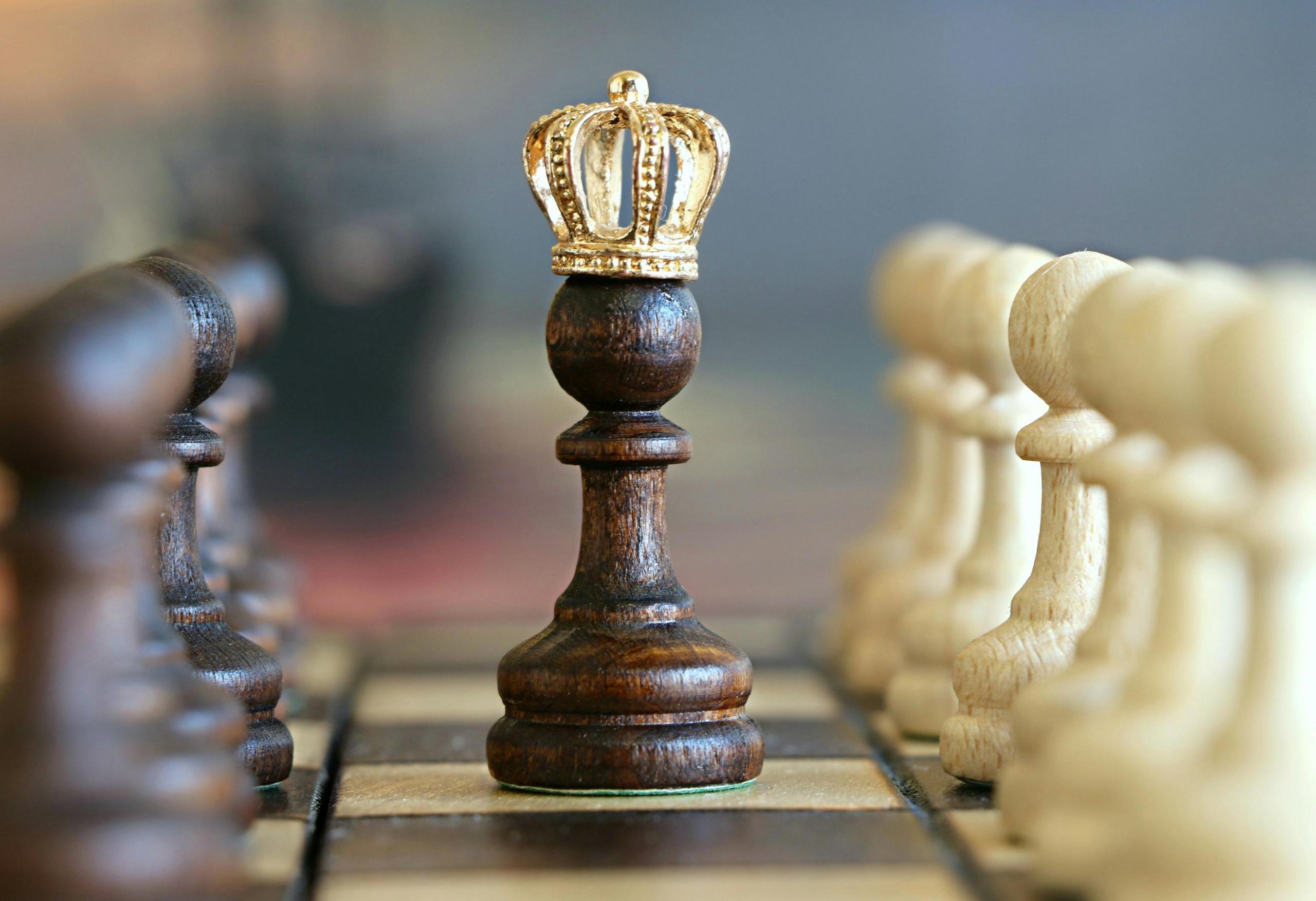 a dark chesspiece stands at the centre of the chessboard with a tiny crown on top.