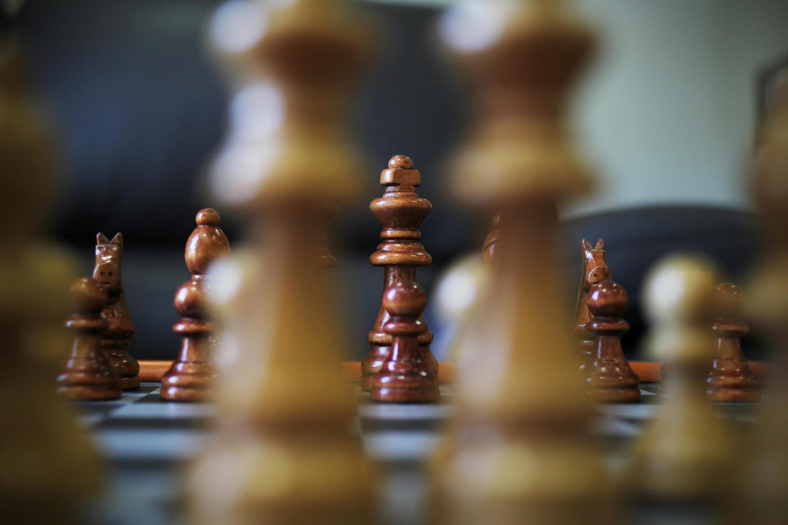 two white chess pieces are in the front of a picture, slightly blurred. Other chess pieces can be seen in the background.