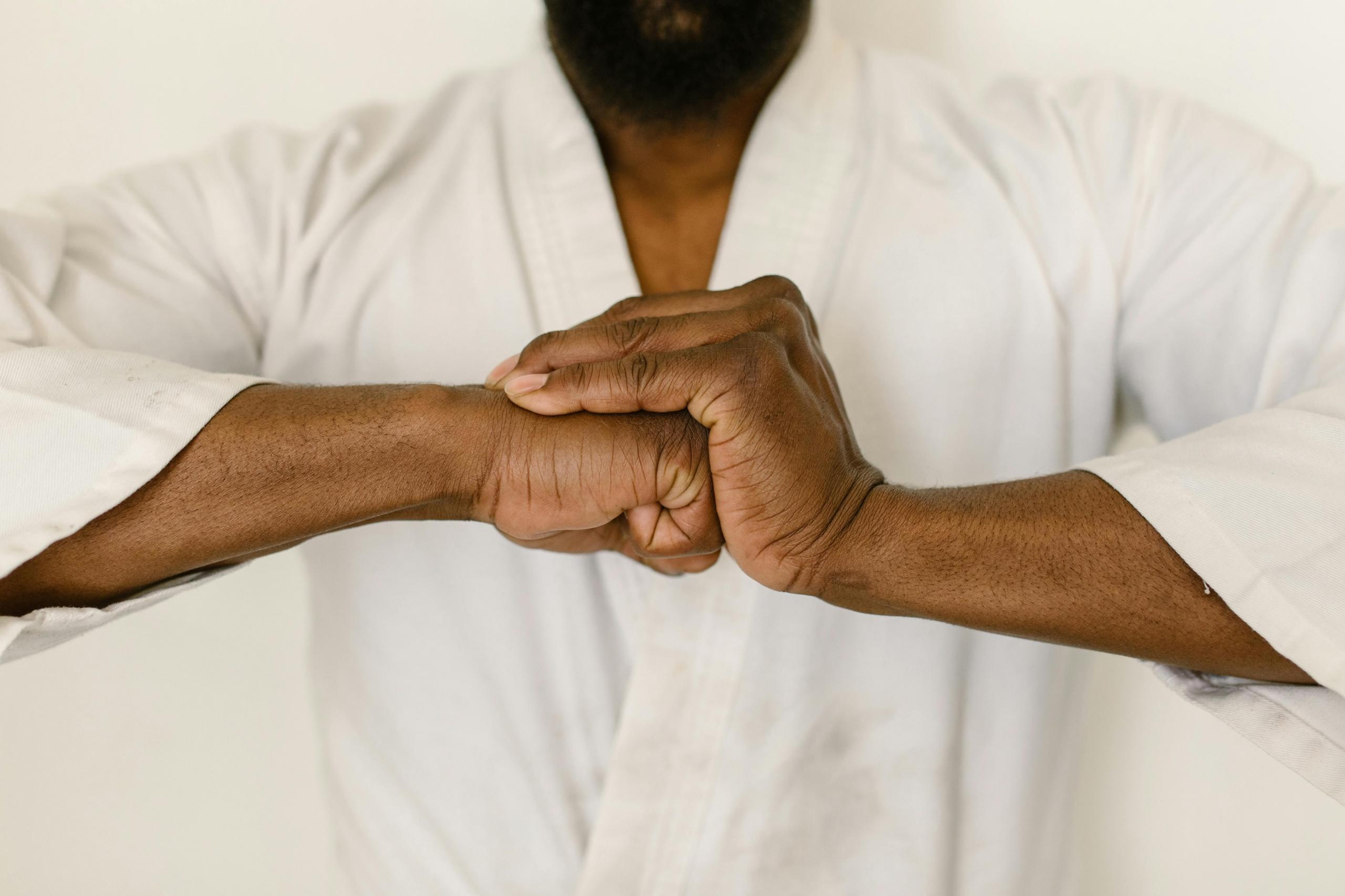 A close-up view of a martial artist in a white gi clasping their hands together in a gesture of focus and commitment. The image emphasizes the strength and determination of the practitioner, highlighting the significance of mental and physical discipline in martial arts training.