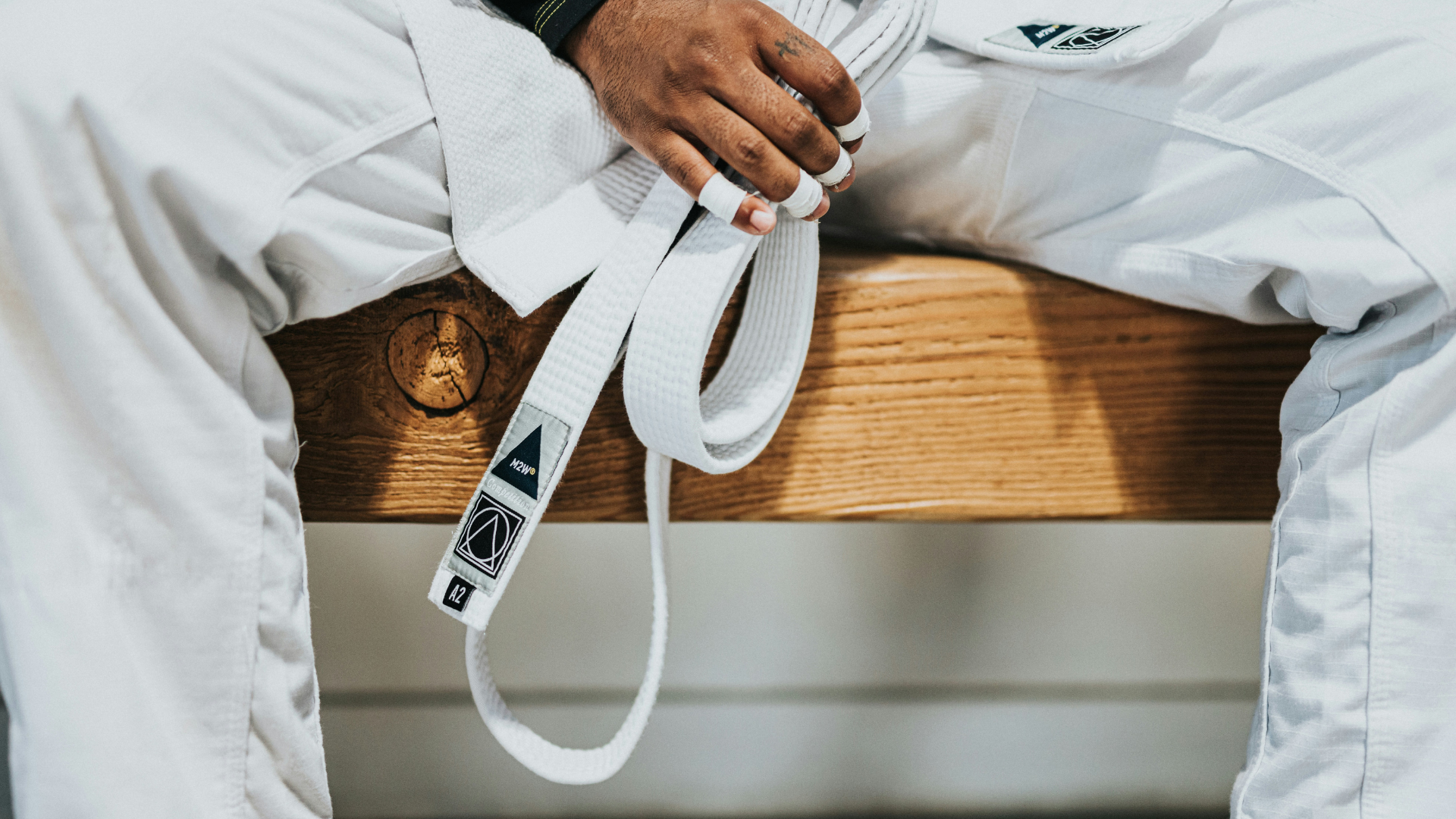 Man sitting on a bench wearing his judogi holding his white belt.