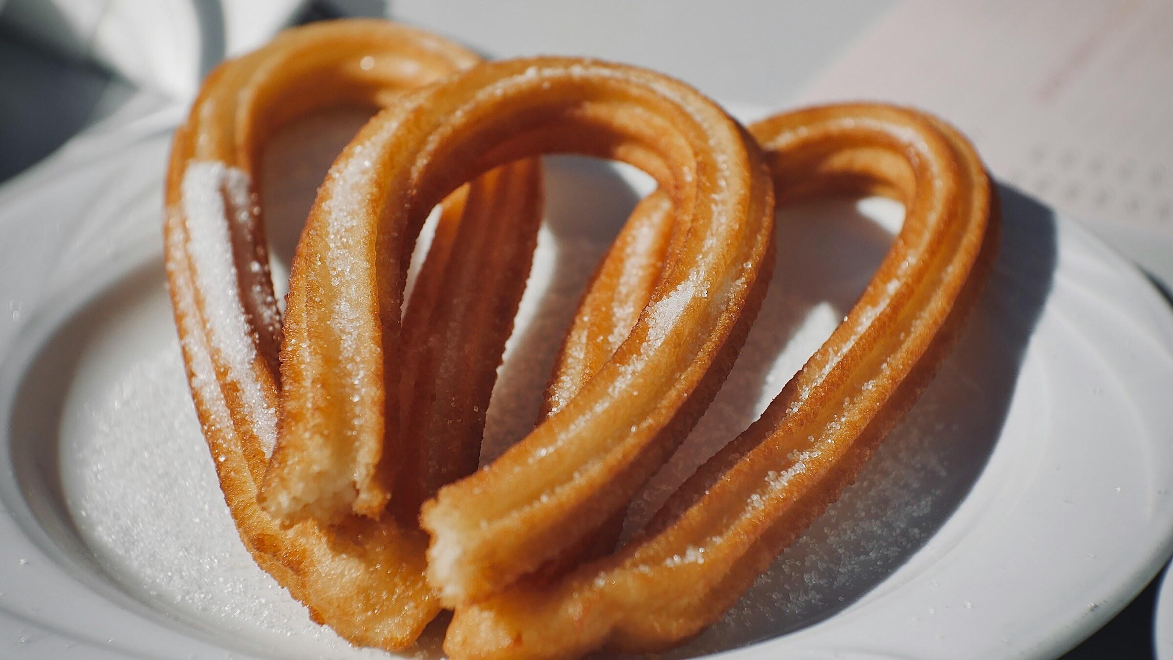 A plate of freshly made churros, lightly dusted with sugar, arranged in a heart shape.
