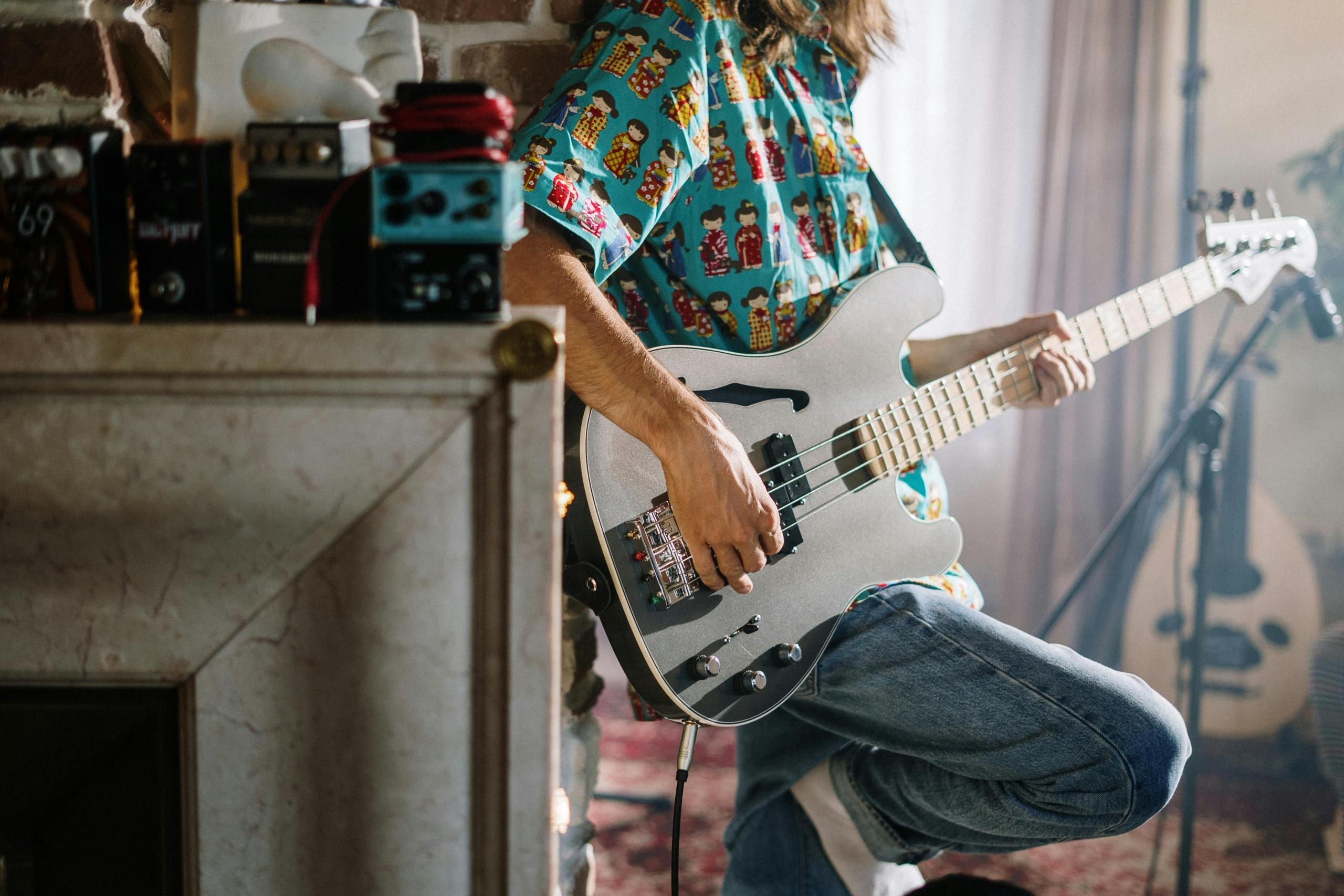 A man leaning against a dresser playing the electric guitar.