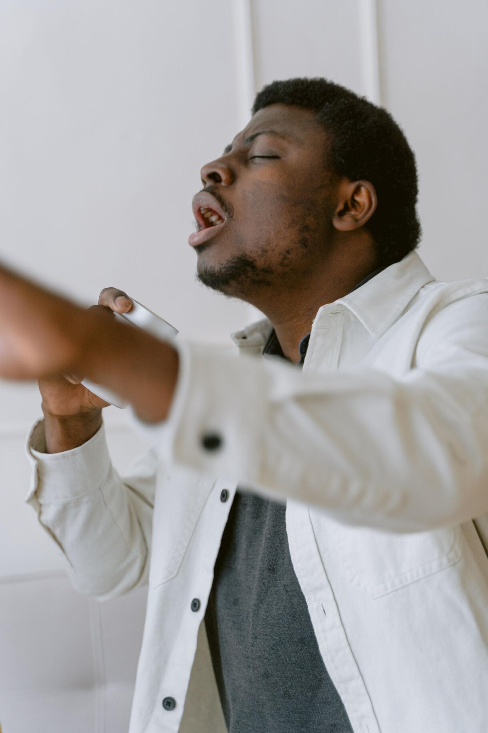 Man in a white jacket holds a microphone and sings with his eyes closed, while a blurred arm crosses the foreground.