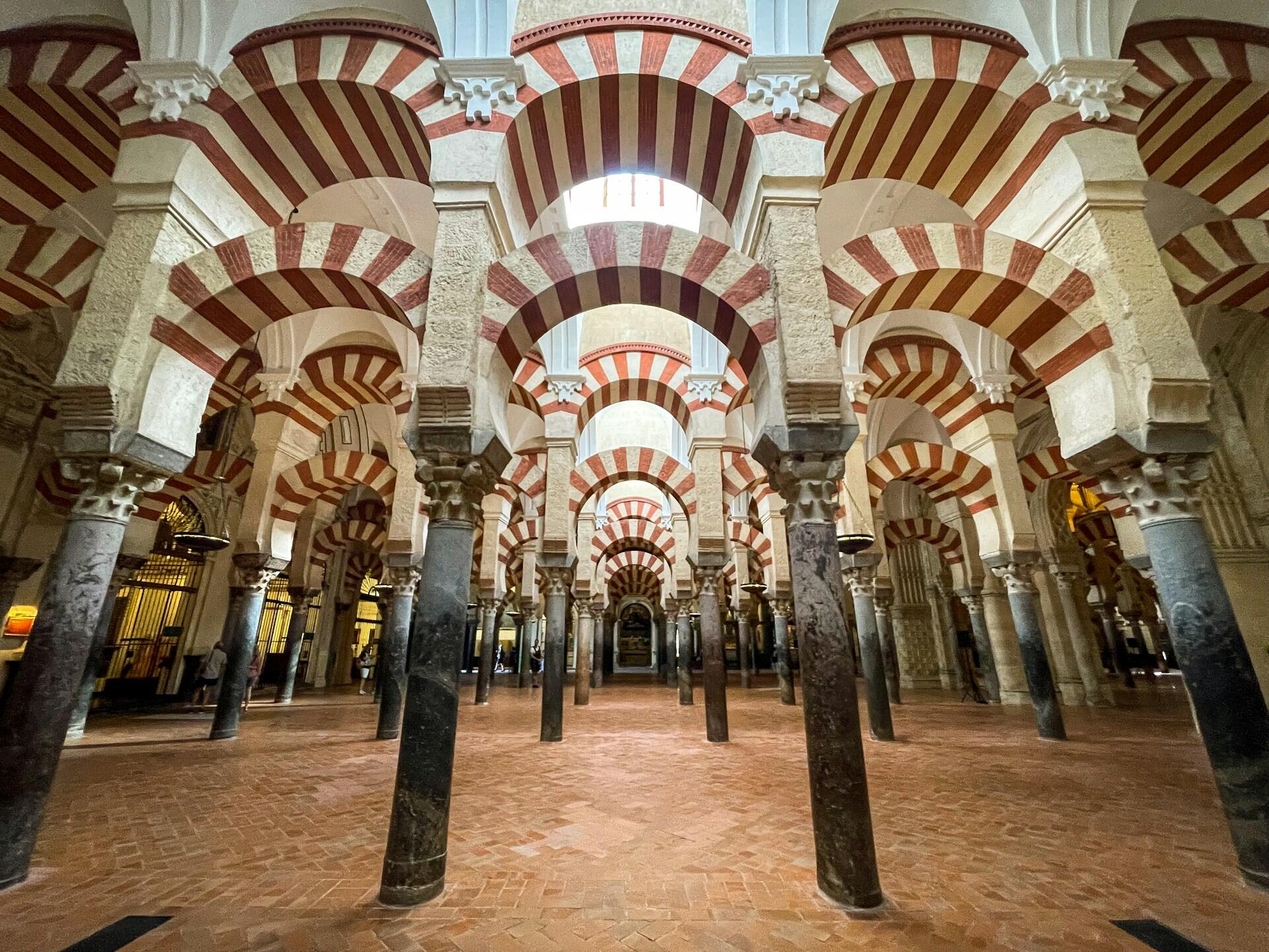 Interior of a historic mosque with striking red and white striped arches supported by ornate columns and a brick floor.