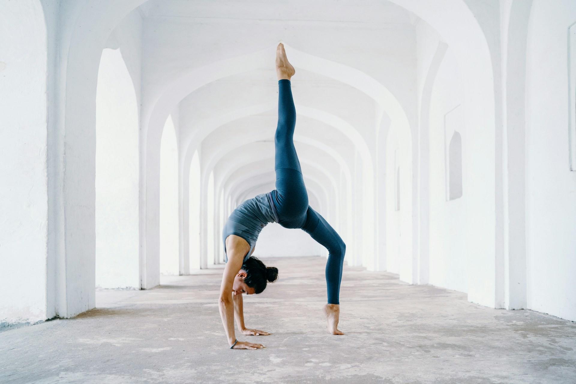 A women doing a backwards bend pose in a empty hallway.