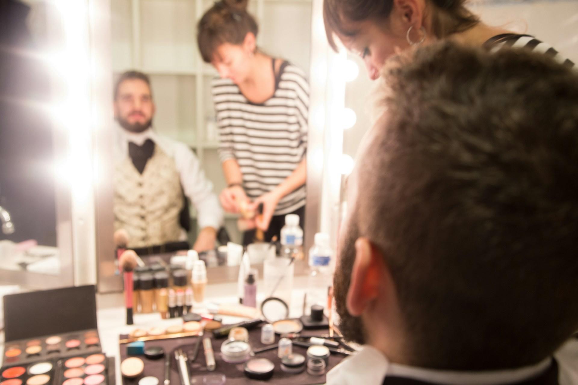 Man in front of the mirror being made up by a professional make-up artist