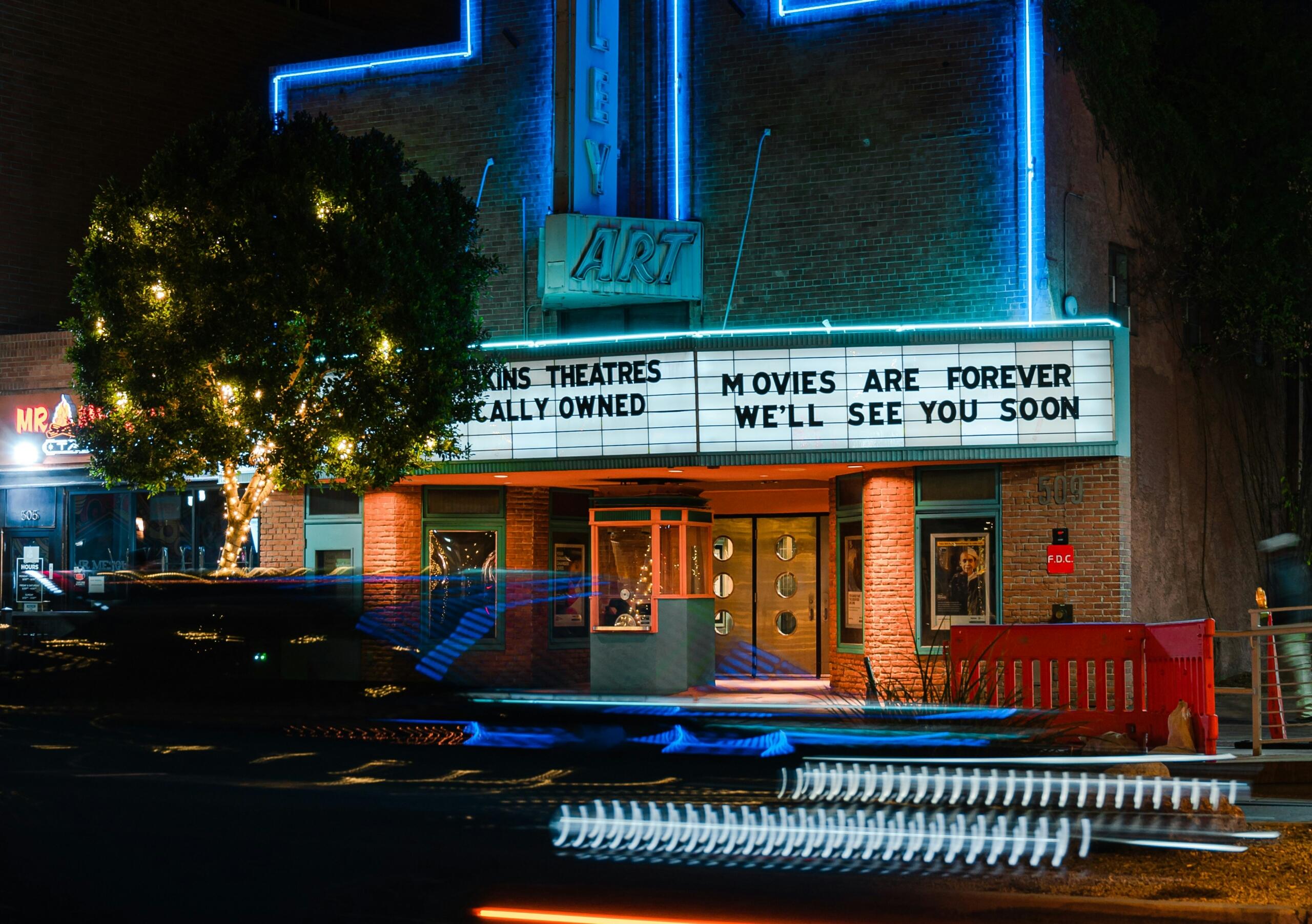 A vintage theater illuminated by neon lights features a marquee reading 
