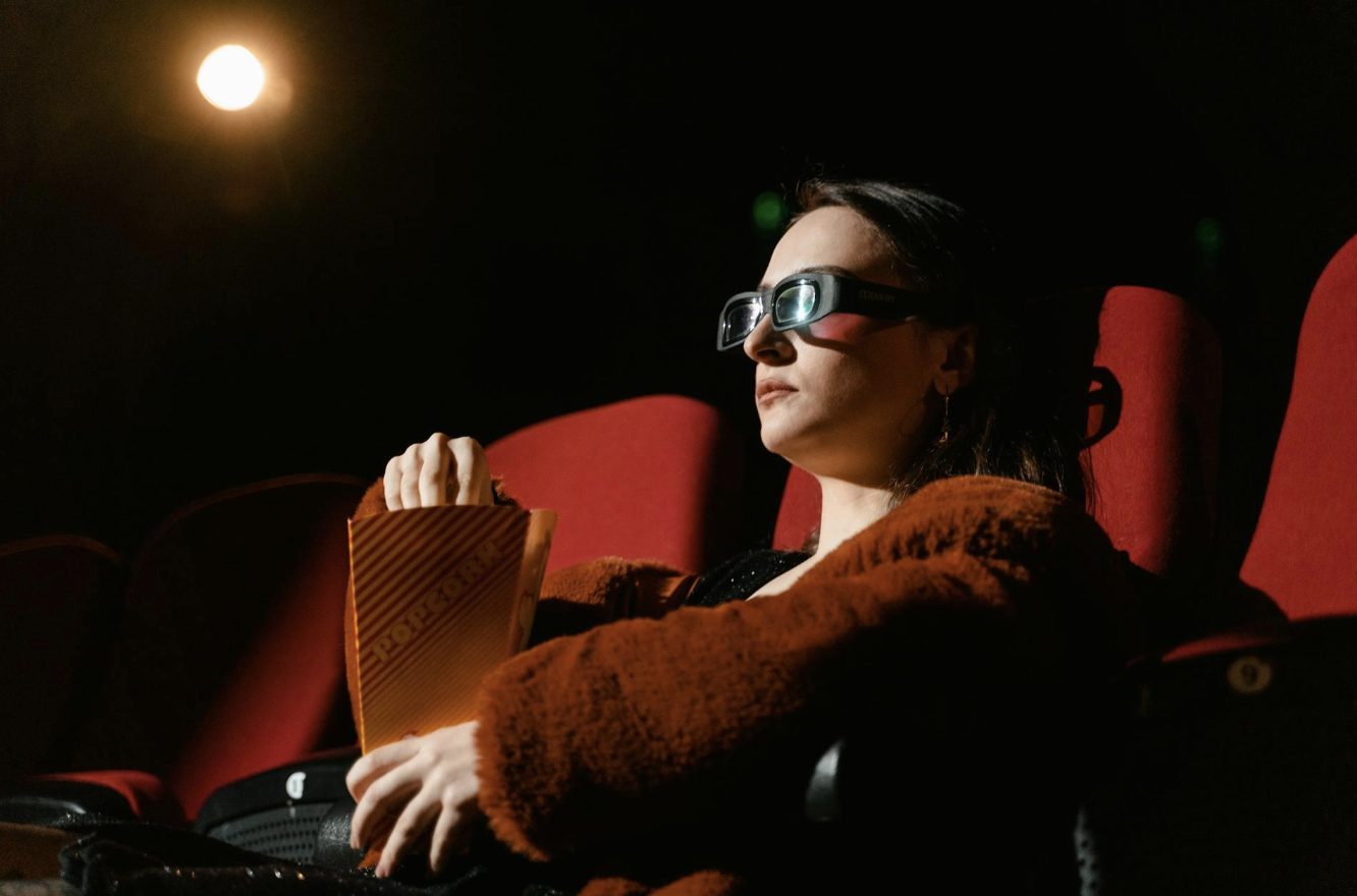 A girl watching movies with 3d glasses on while eating popcorn.