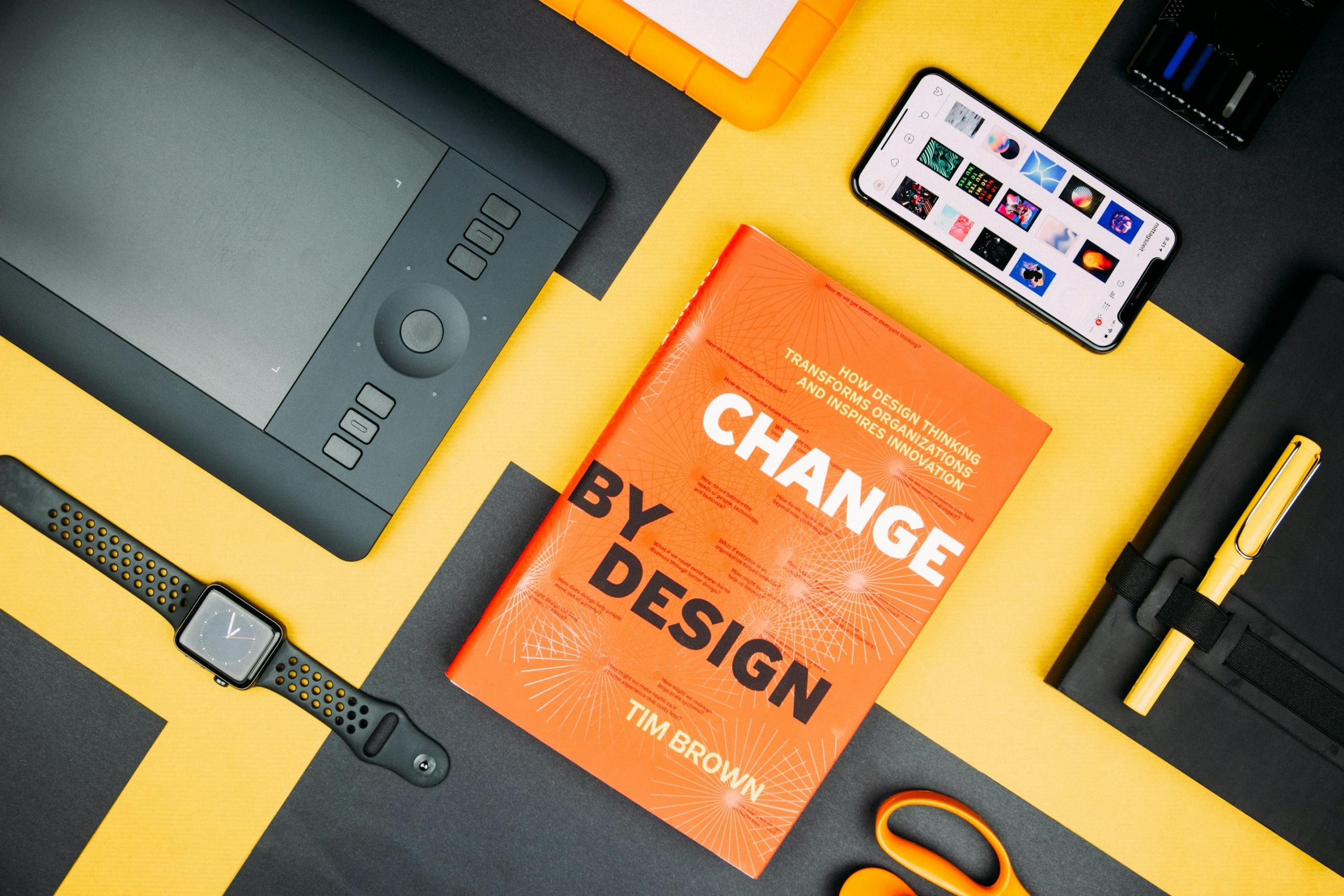 A book about graphic design on a desk besides a drawing tablet, scissors and other objects.