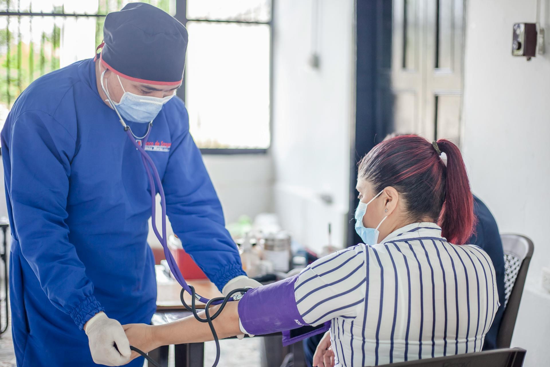 A health care practitioner taking a patient's blood pressure while wearing a mouthpiece.